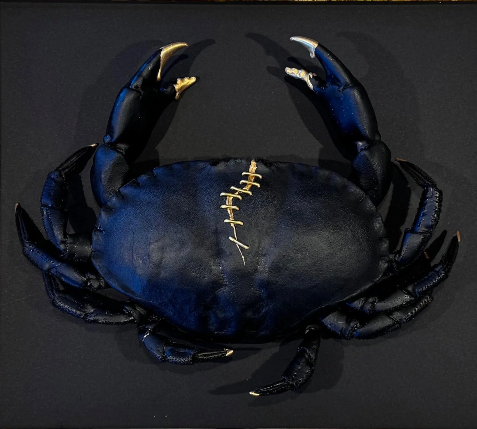 Black crab with gold accents on claws and a stitched pattern on shell, placed on a black background.