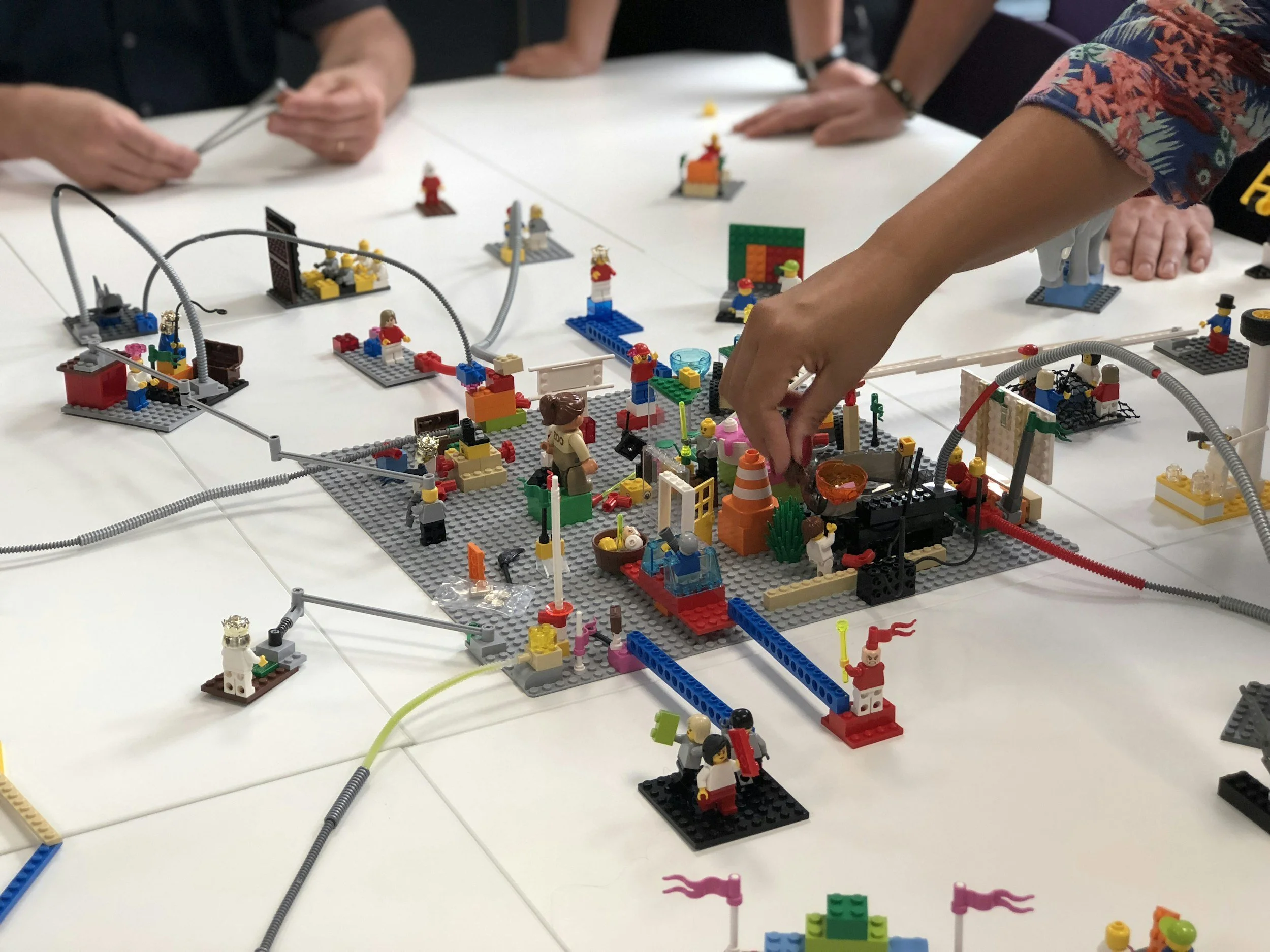 People playing with LEGO bricks on a table, building a colorful structure with various LEGO characters and accessories.
