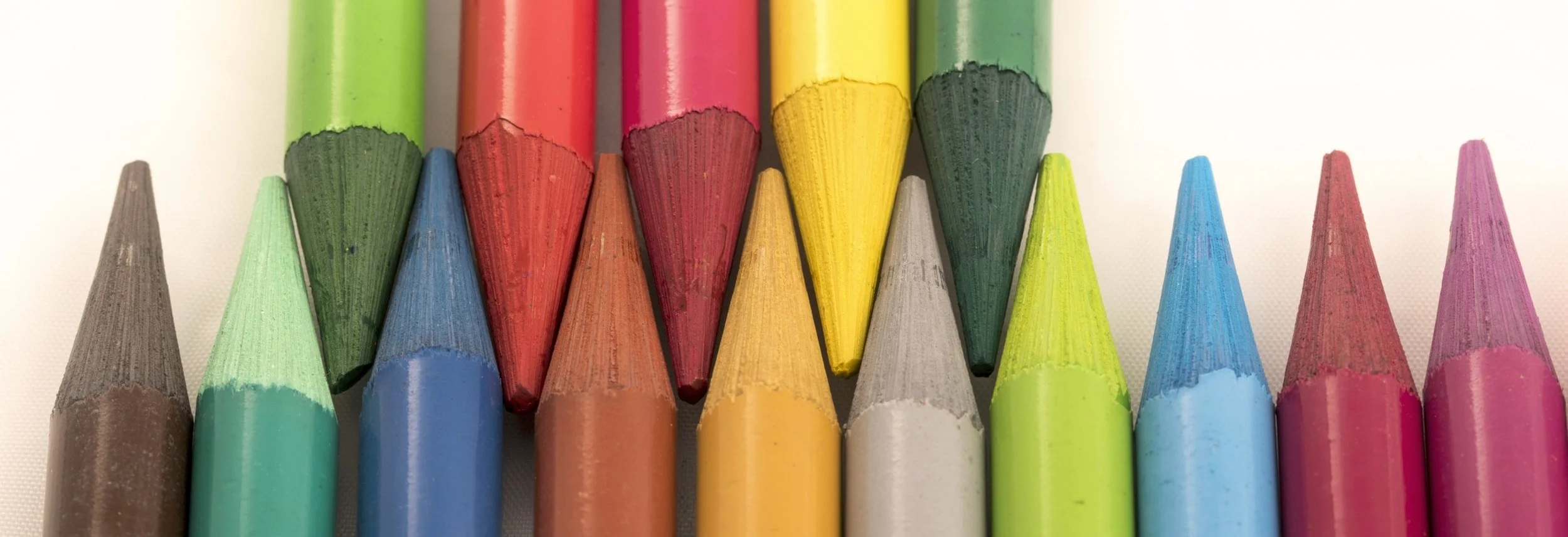 Close-up of colorful crayons arranged in a row, featuring red, yellow, green, blue, pink, and gray colors.