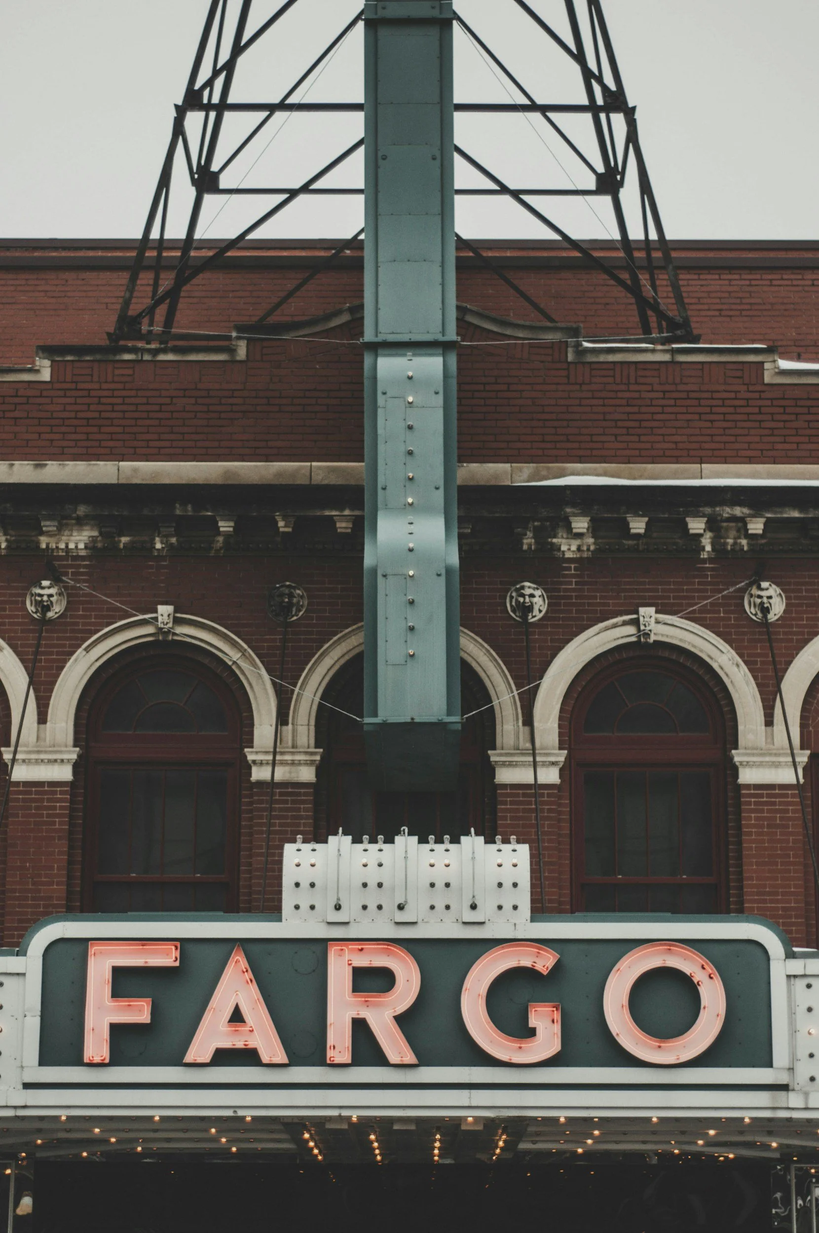 Fargo theater marquee sign with glowing pink letters, above a brick building with arched windows and a metal tower structure.