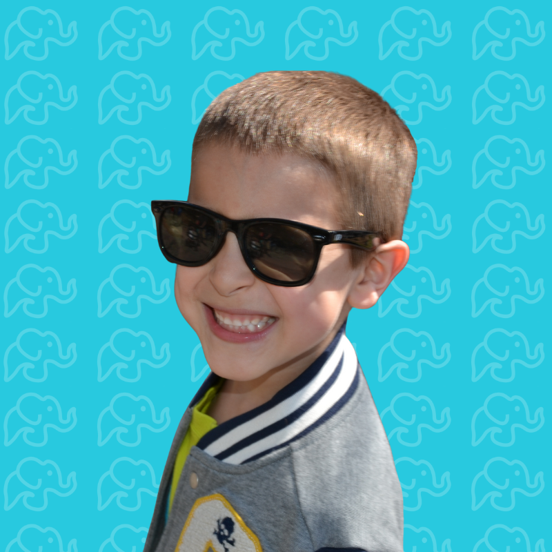 Smiling young boy wearing sunglasses and a gray jacket with a varsity stripe