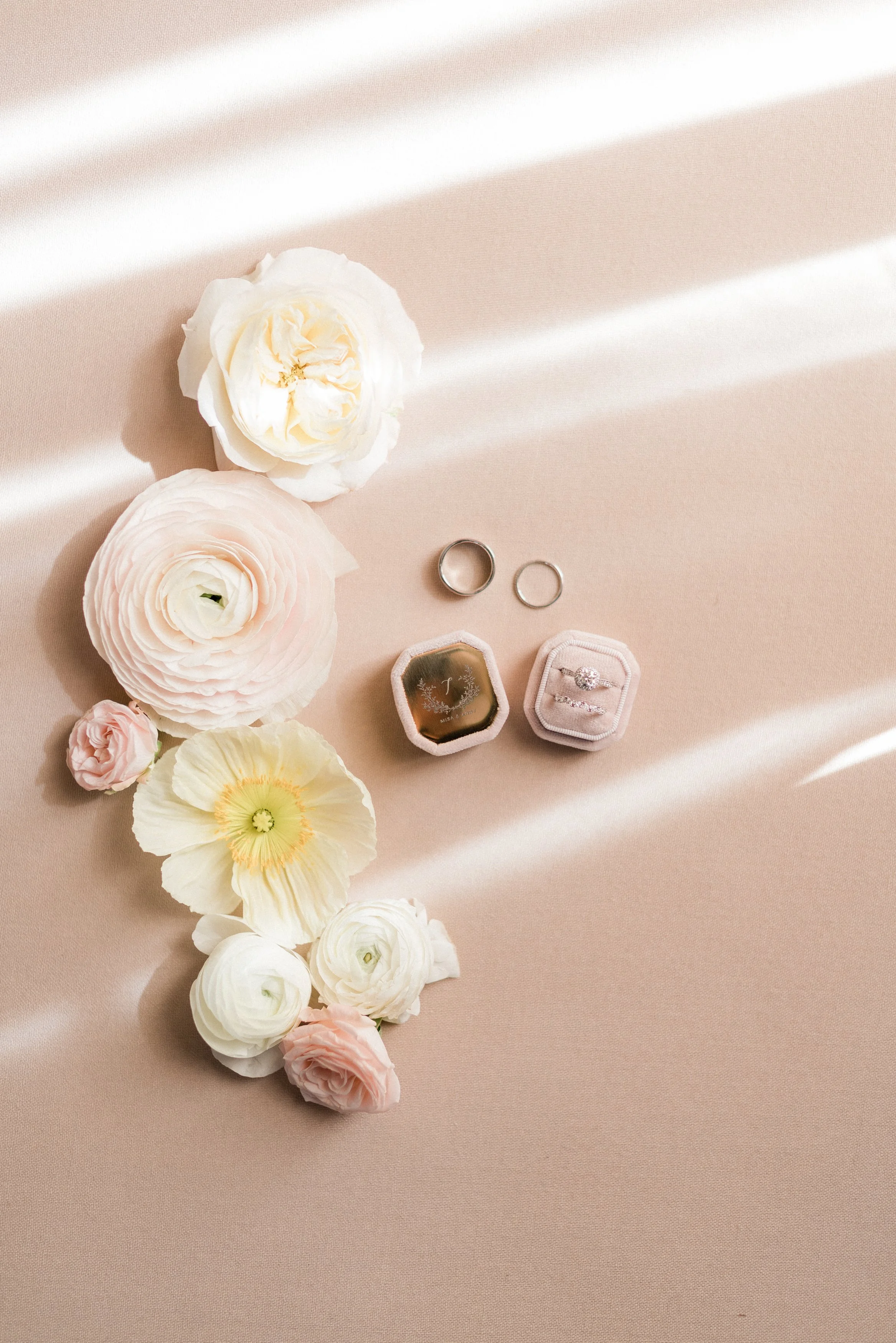 Silver wedding rings, wedding bands, engagement ring in a pink velvet ring box, and jewelry box on a peach fabric with pastel flowers.