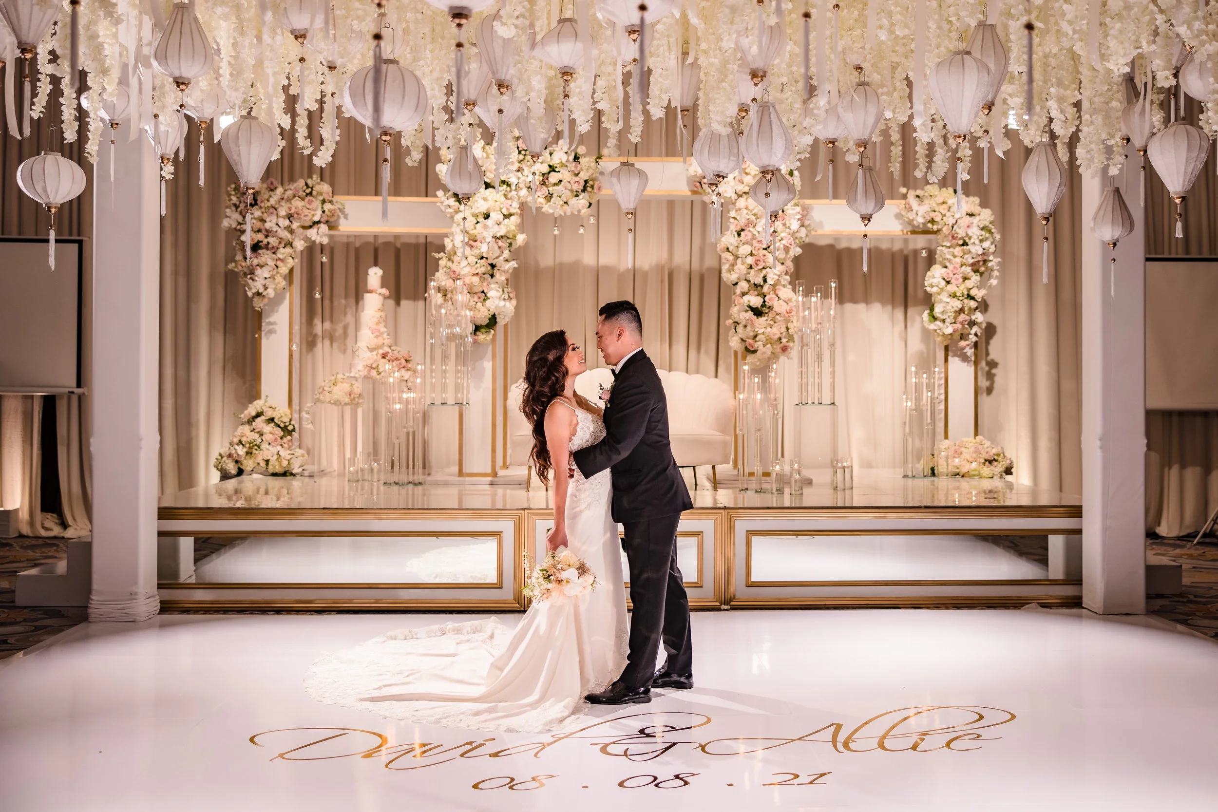 A bride and groom sharing a dance on a decorated wedding stage with hanging lanterns and floral arrangements.