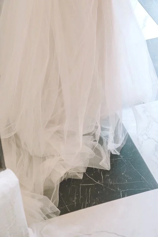 A close-up of a white tulle fabric curtain hanging down over a black marble floor with white veining.
