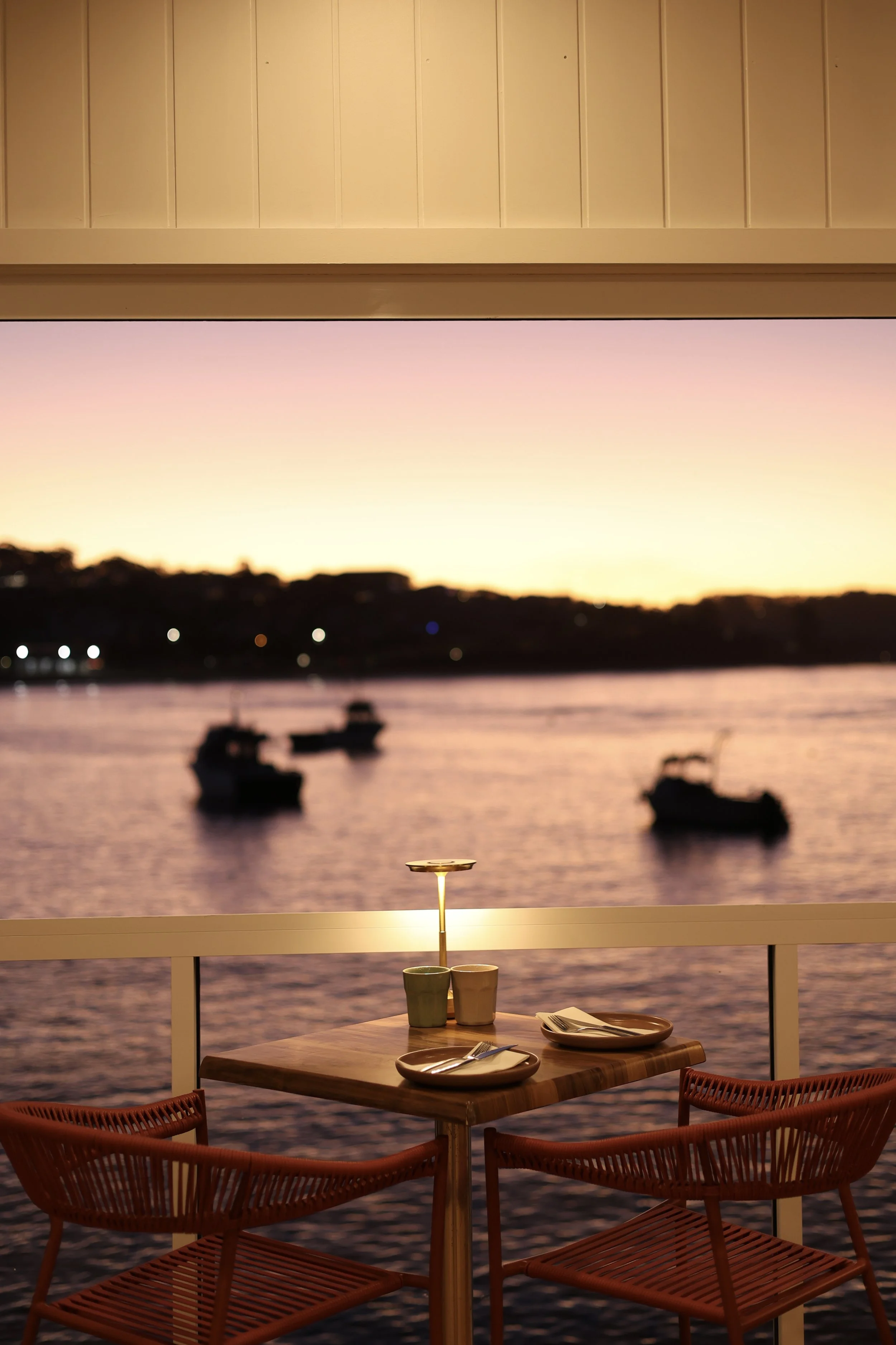 dinging table set for two with sun setting over the water in background