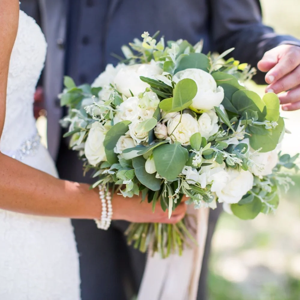 Close-up of bride holding a bouquet of white roses and greenery beside groom during ceremony.