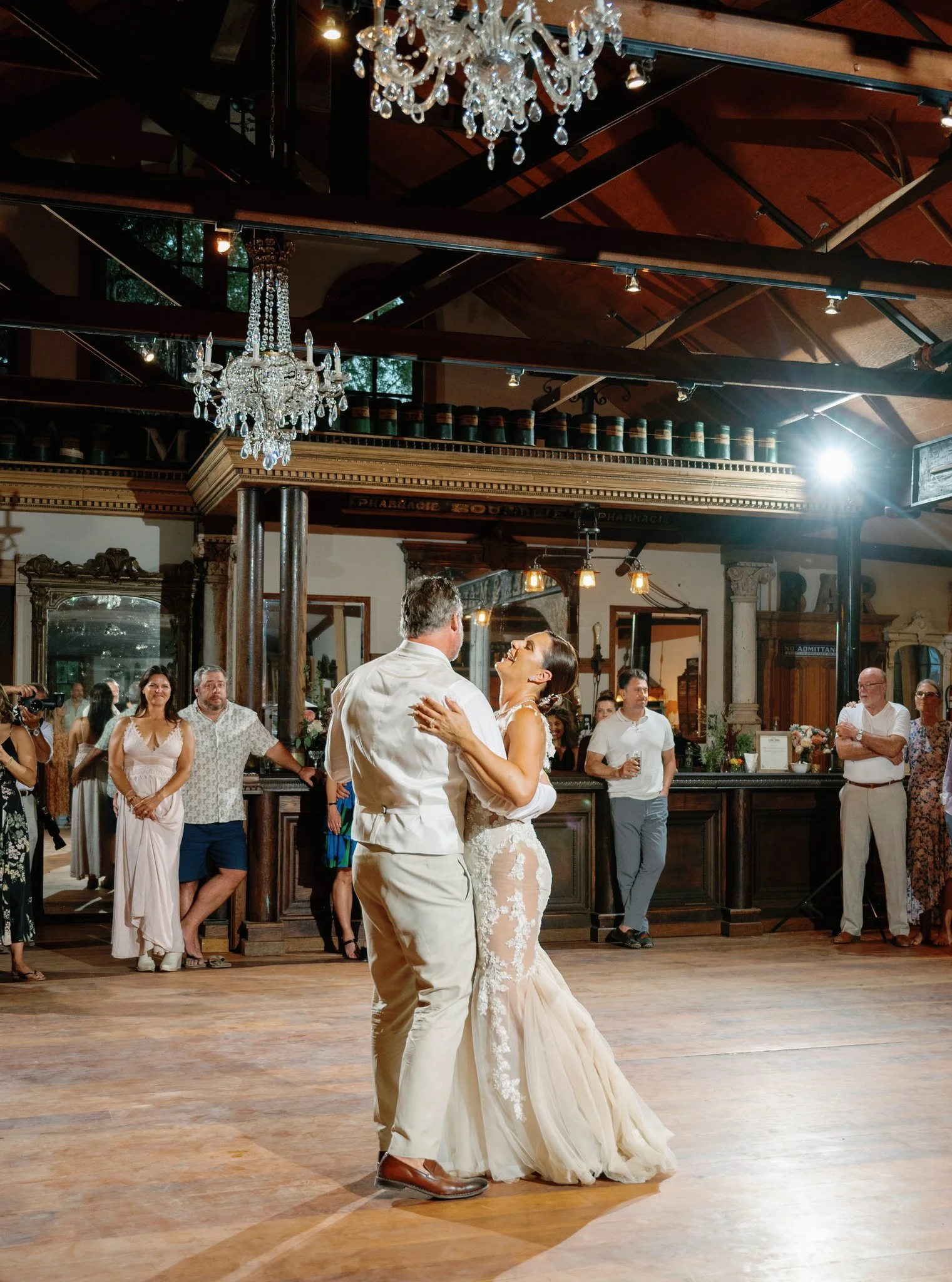 Bride and groom dancing together at wedding reception surrounded by smiling guests.