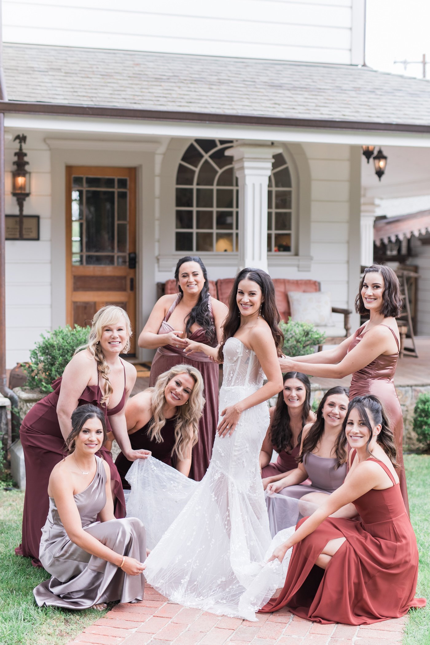 Bride and bridesmaids smiling and posing outside a house, holding the bride’s train at Triple S Ranch wedding venue in Napa California