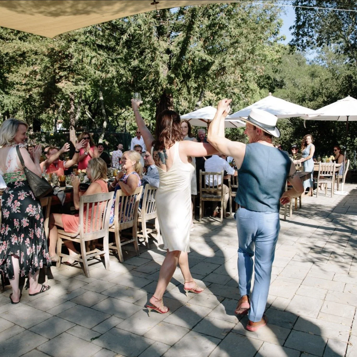 People celebrating outdoors at a wedding at Triple S Ranch, with a woman and man dancing in front of a group of seated guests under umbrellas.