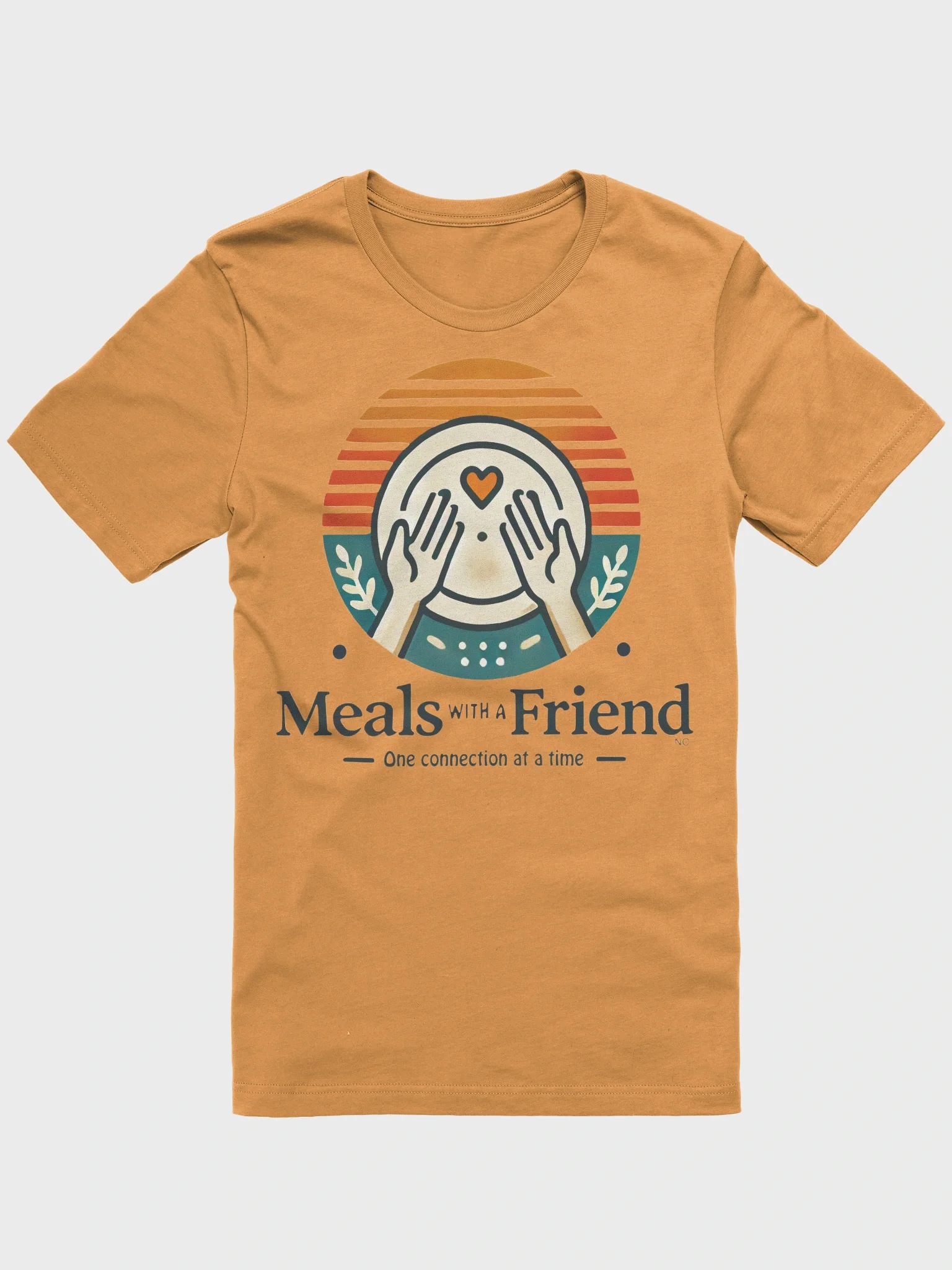 Tan T-shirt with graphic of person covering face with hands, heart on forehead, sunset background, and text 'Meals with a Friend - One connection at a time'.