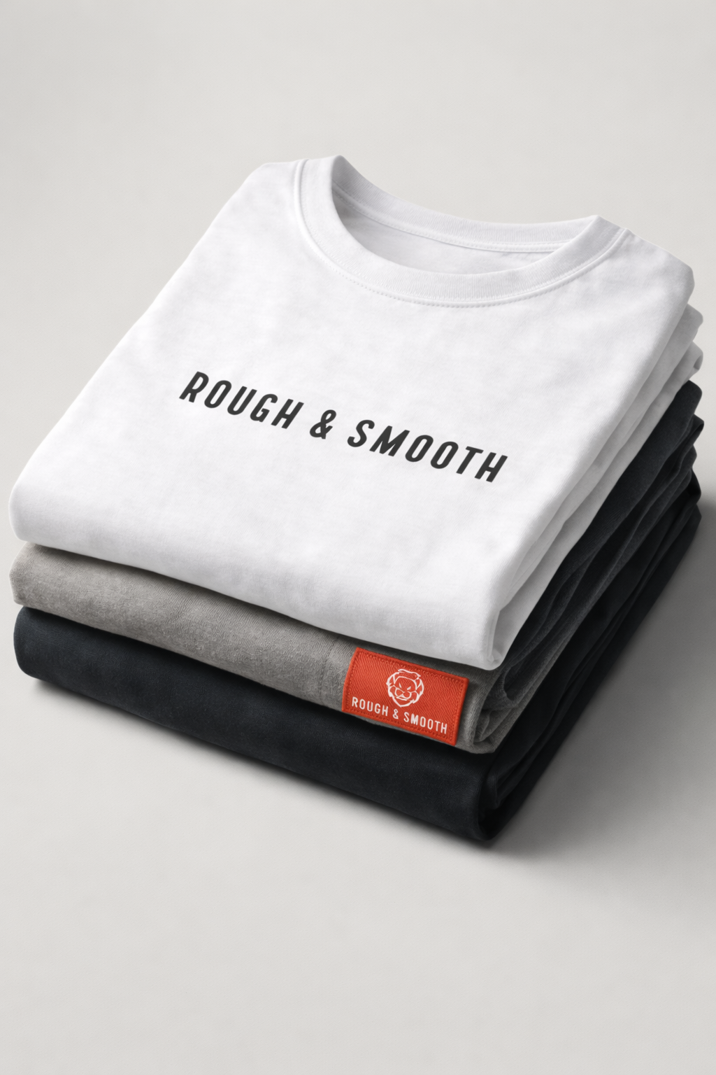 Folded Rough & Smooth T-shirts in white, gray, and black, featuring the brand logo and red tag details.