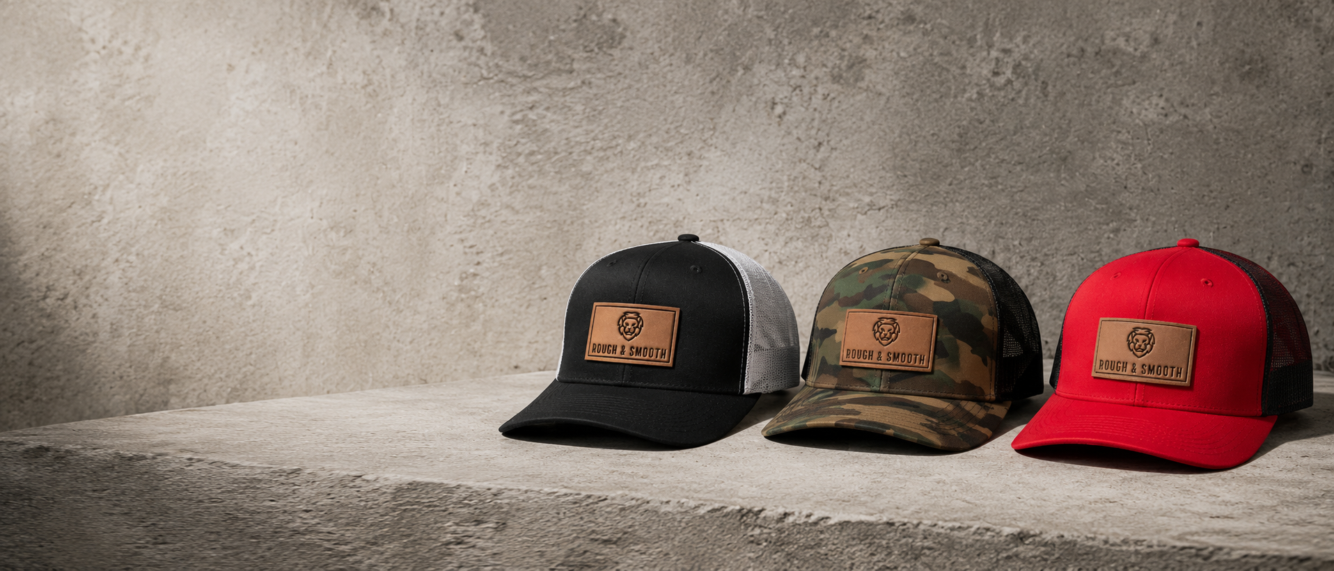 Rough & Smooth premium caps in black, camouflage, and red displayed on a concrete ledge.