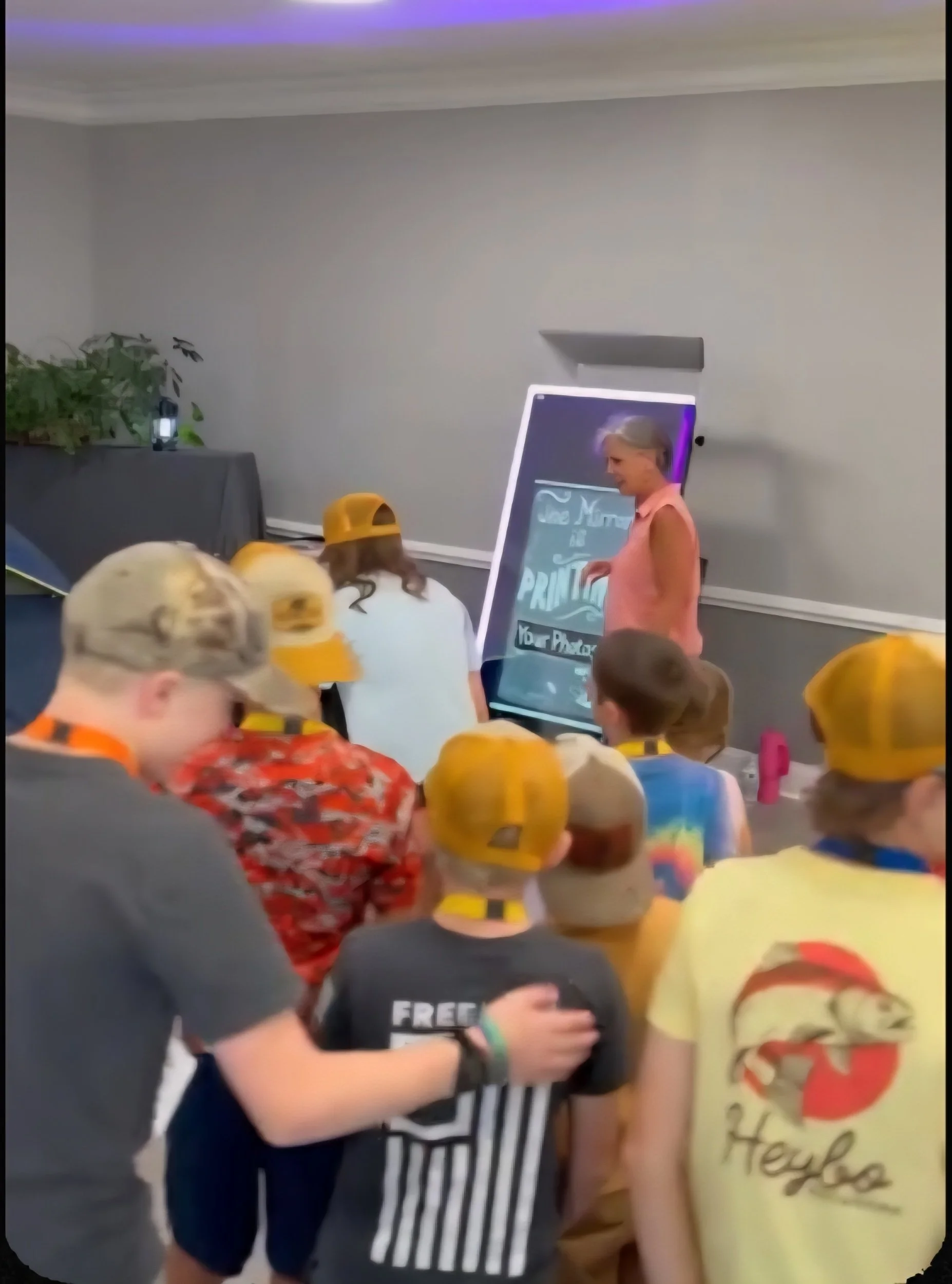 Children watching a woman write on a large touchscreen display during an indoor event.