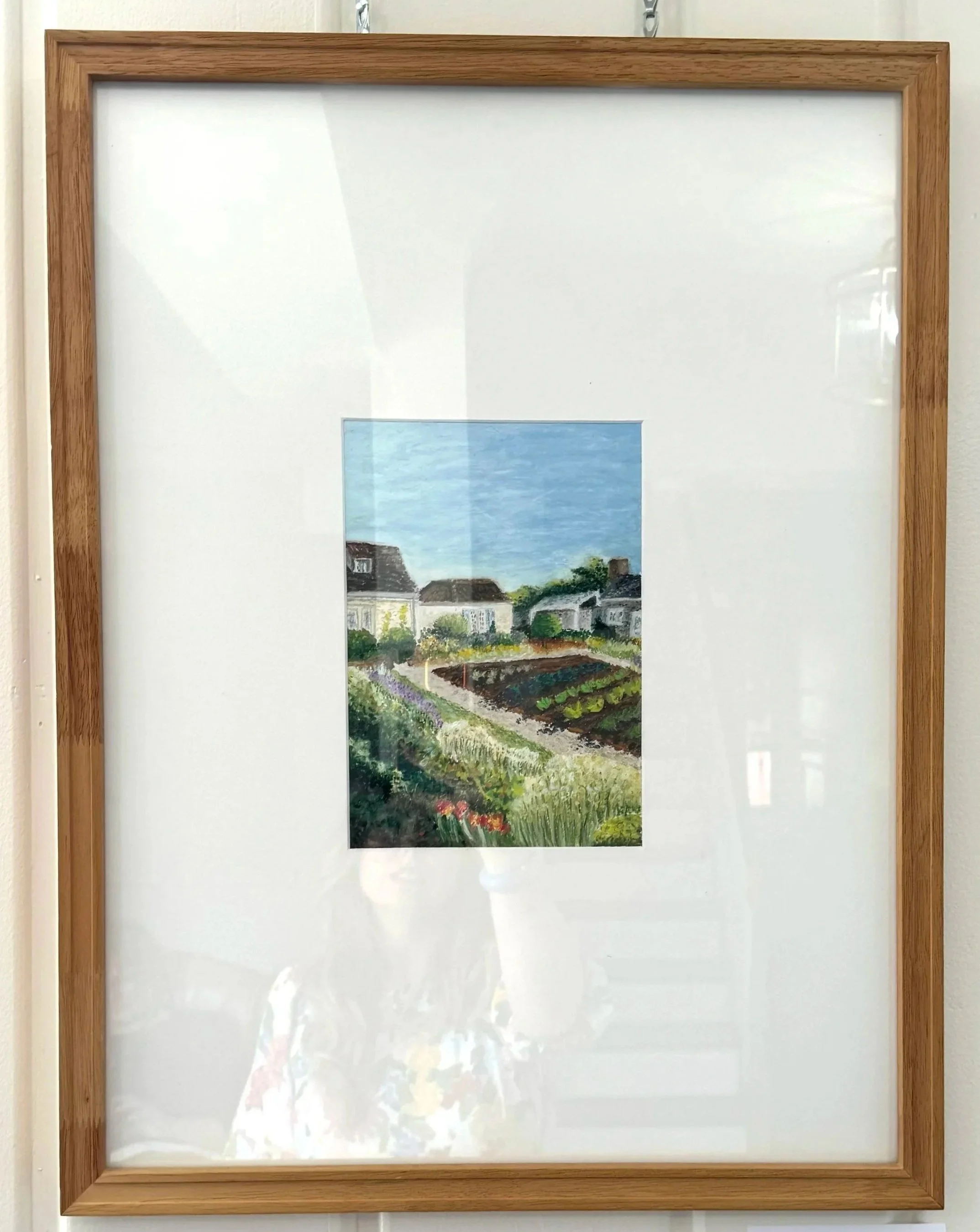 Framed miniature painting of a garden with houses and a blue sky.