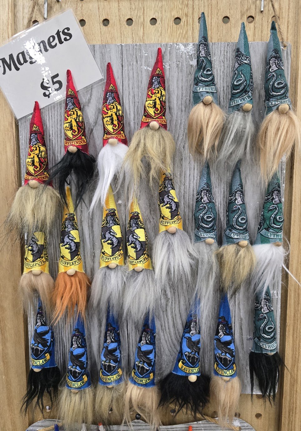 Display of wizard hats featuring Harry Potter house logos and names, with colorful fake beards and long hair.