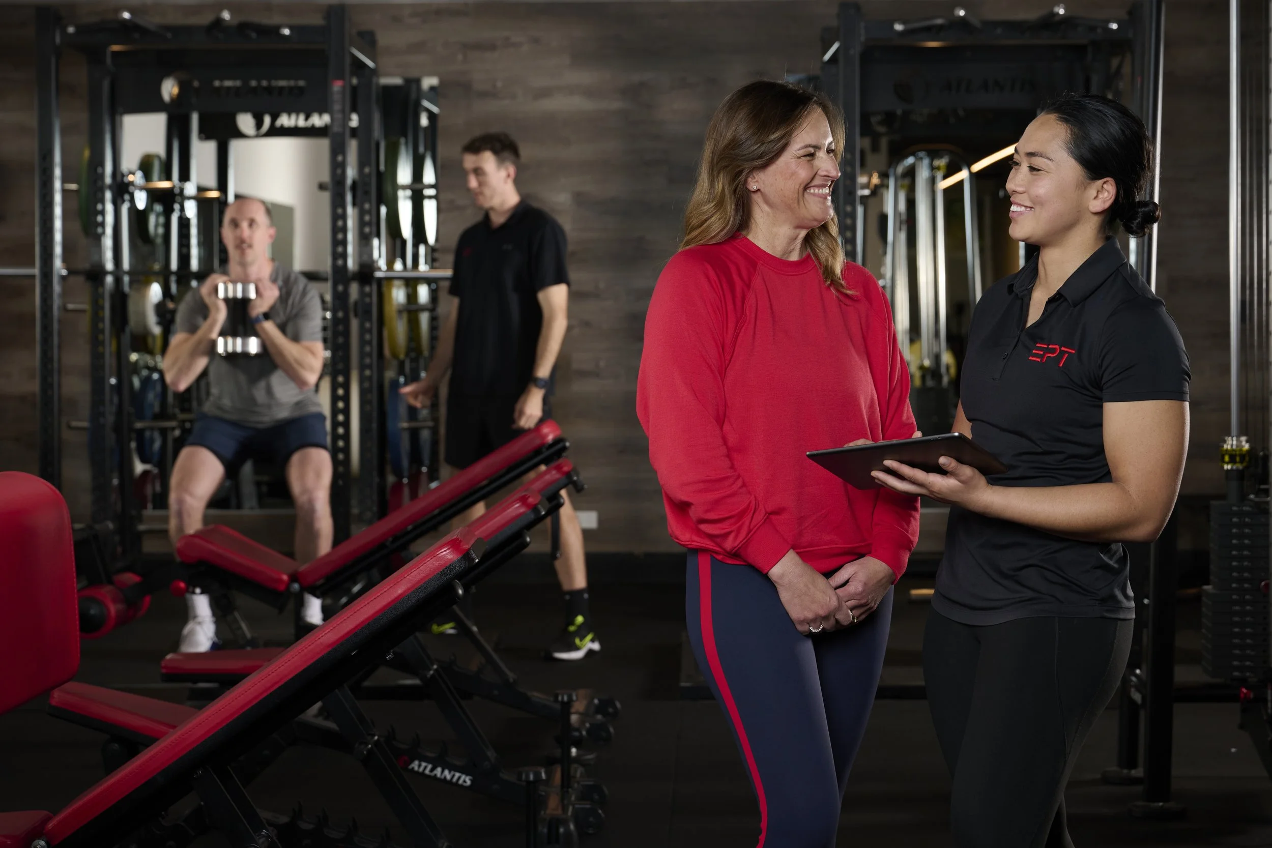 EPT Trainer Sophie smiling at EPT Client before her session, showing her the detailed exercise plan