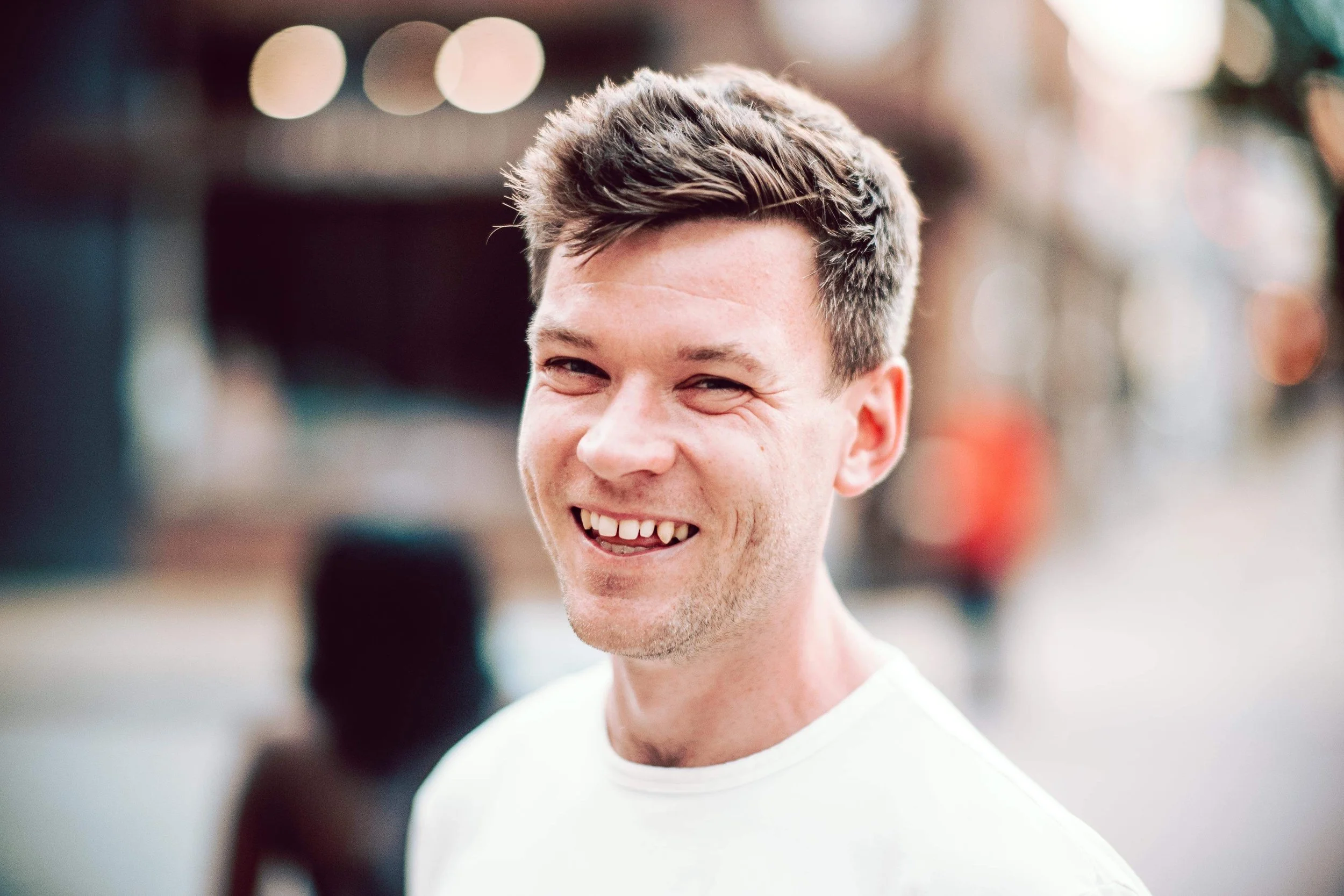 A young man with short dark hair smiling outdoors.