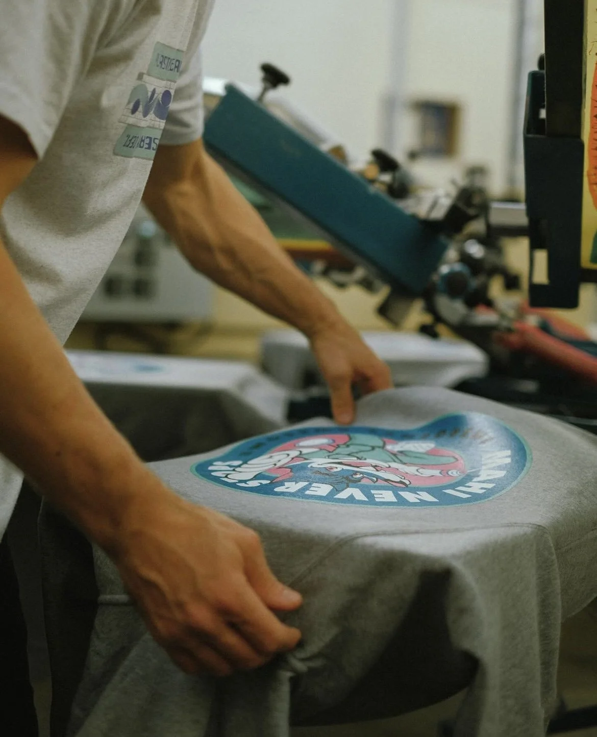 A person is pressing a design onto a gray T-shirt with a heat press in a printing workshop.
