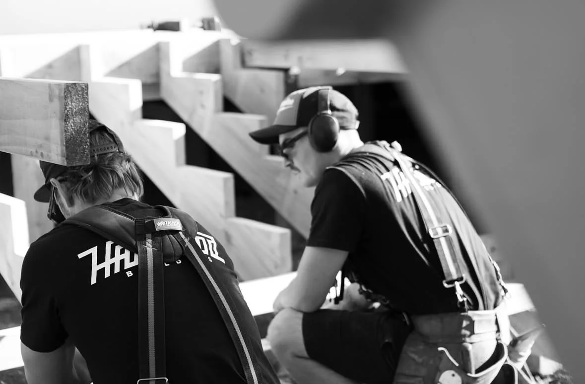 Two young men with backpacks and headphones sitting outdoors on wooden steps.