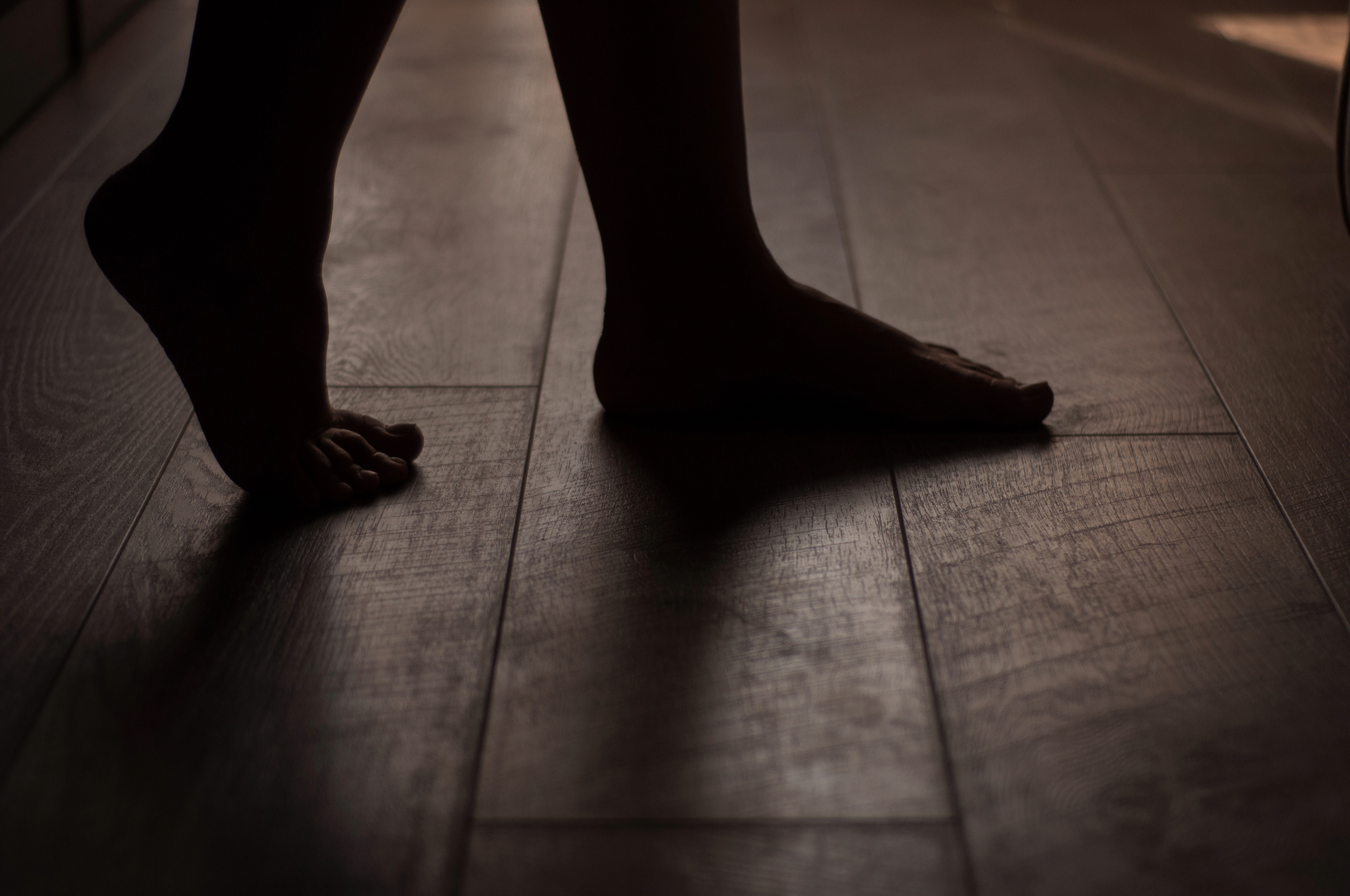 Close-up of a child's bare feet on a wooden floor, with a shadow cast to the side.