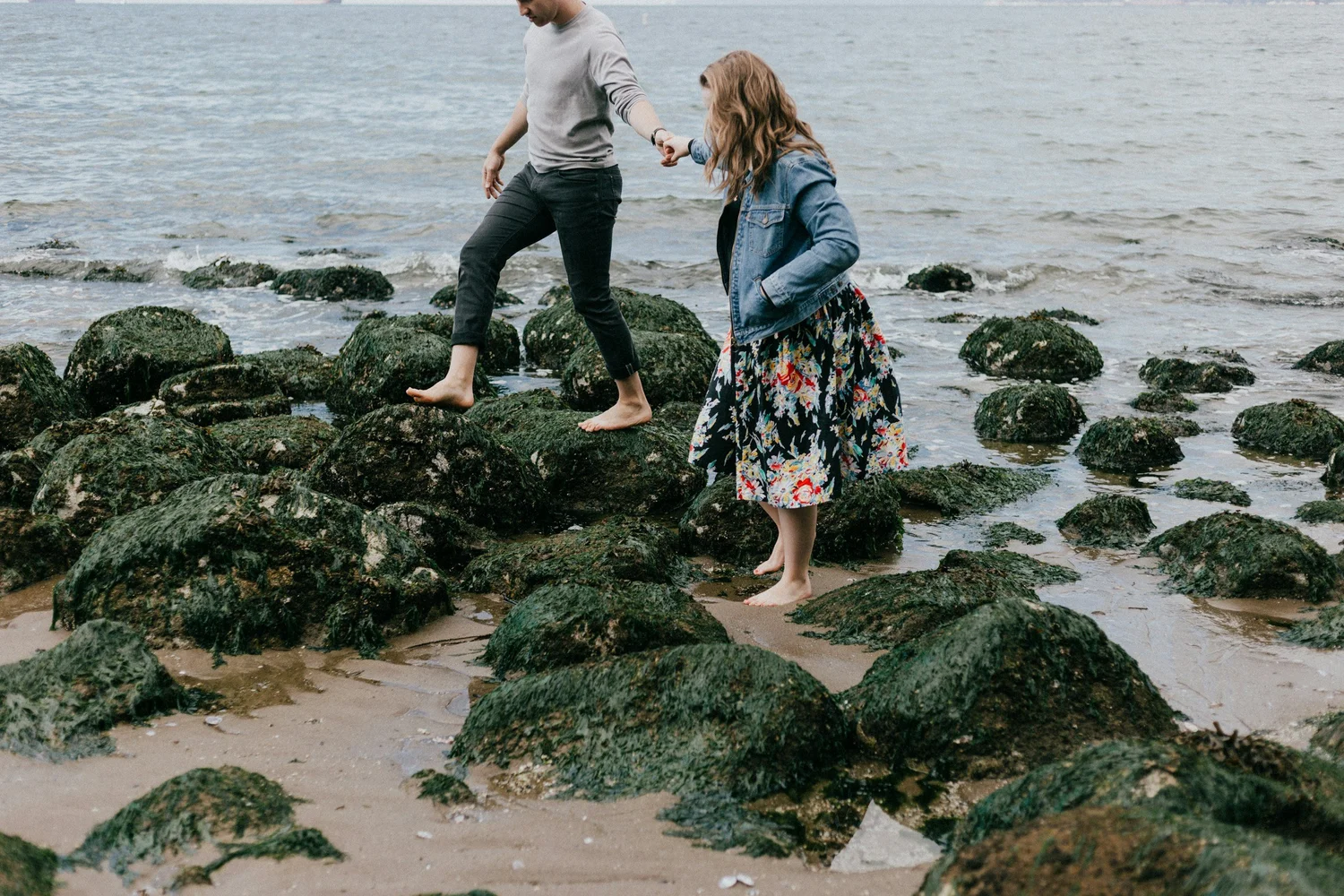 A couple holding hands on the rocks at the beach