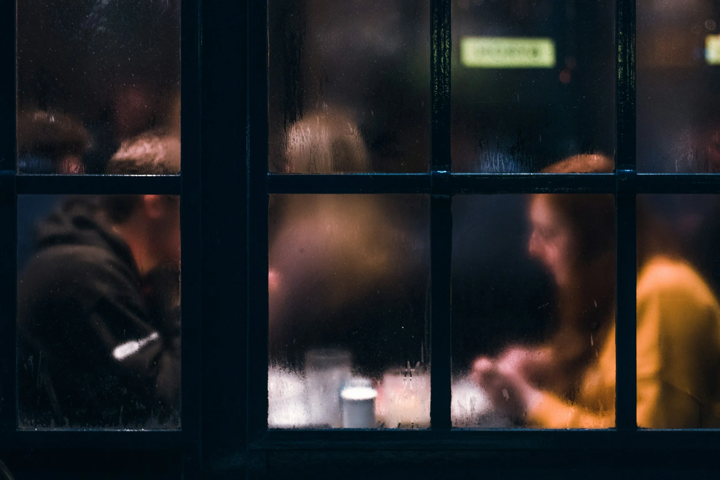 Two people sitting at a table visible through a foggy glass window in a dimly lit setting.