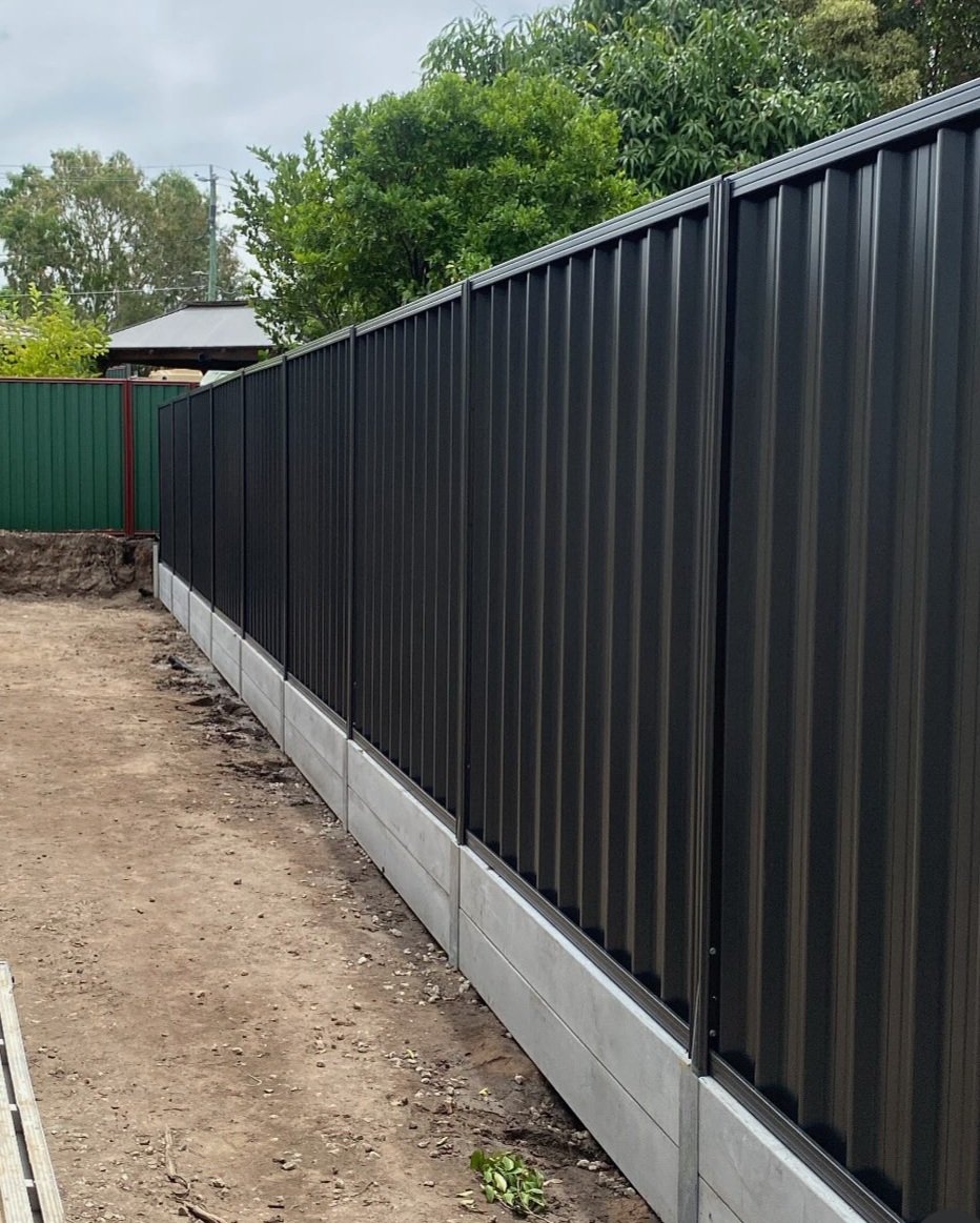 Cement retaining wall as a base with a Colorbond fence provides a modern look that you can either run turf to or put in a garden.