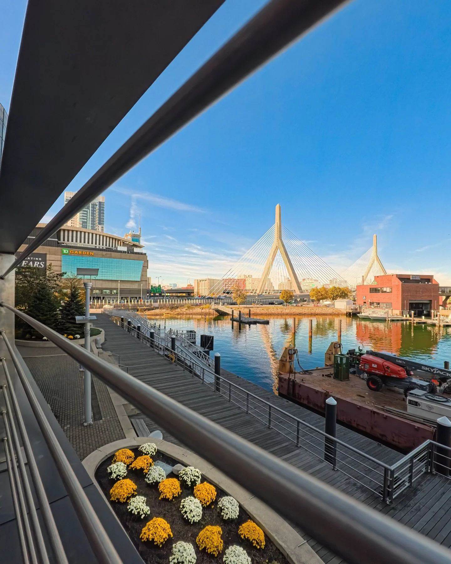 Morning lines that lead straight to the Zakim 👀 

The boardwalk is quiet, the water is glass, and the cables glow in that first burst of light. I framed this from Lovejoy Wharf so the steel rails pull your eye past TD Garden to the bridge, with pops