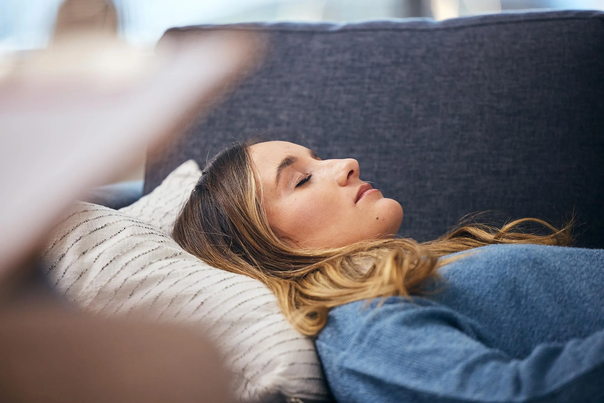 A woman with long hair resting peacefully on a pillow, lying on a sofa with her eyes closed.