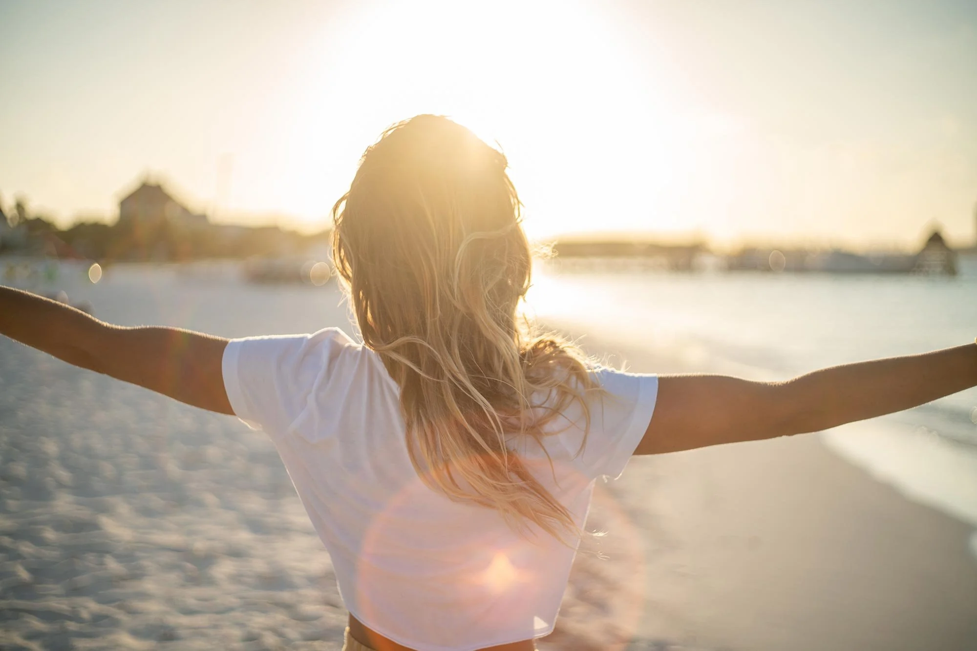 Woman standing on beach with arms outstretched during sunset.