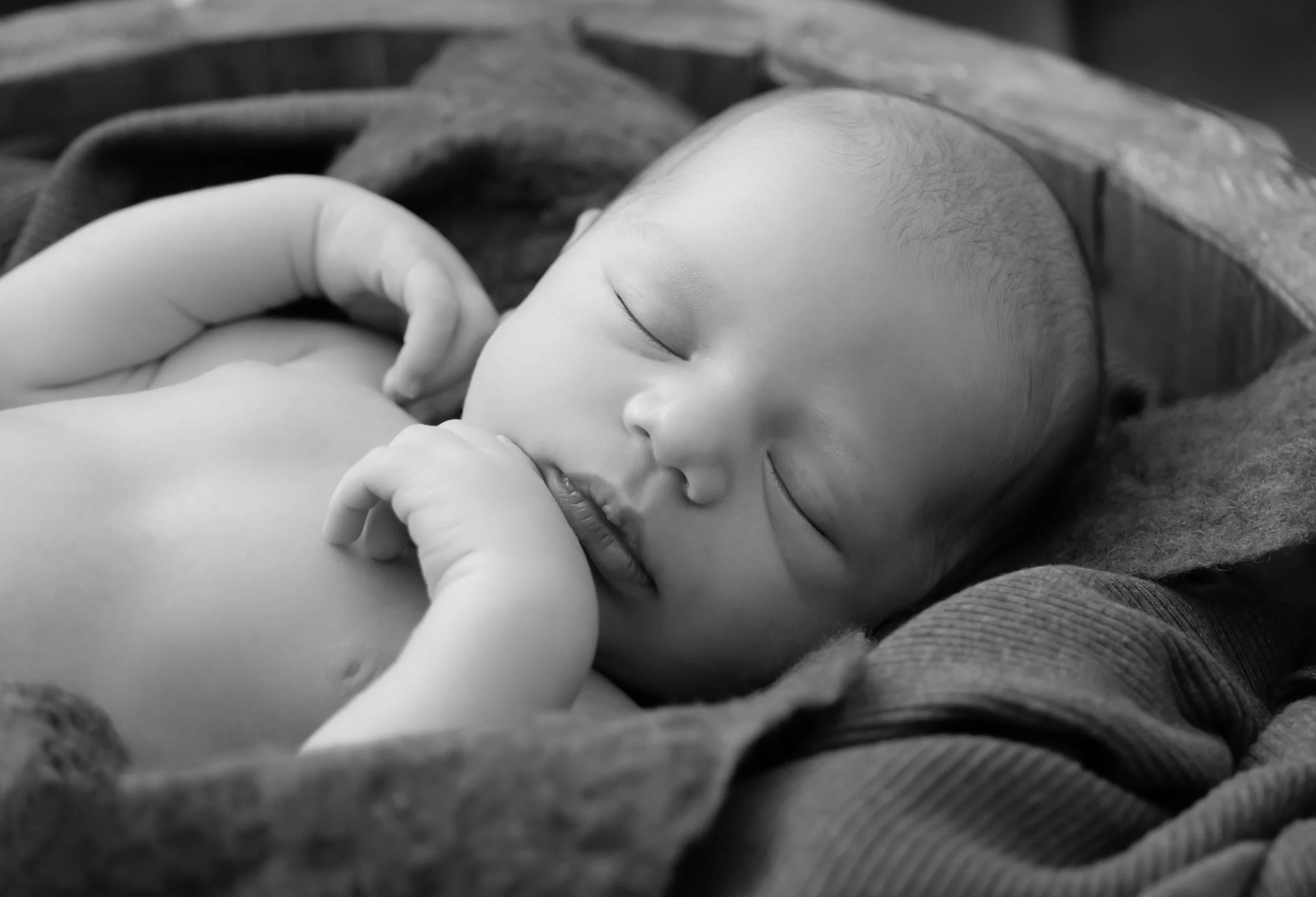 A sleeping baby with eyes closed, lying on a soft surface, with an adult's hand gently touching its head.