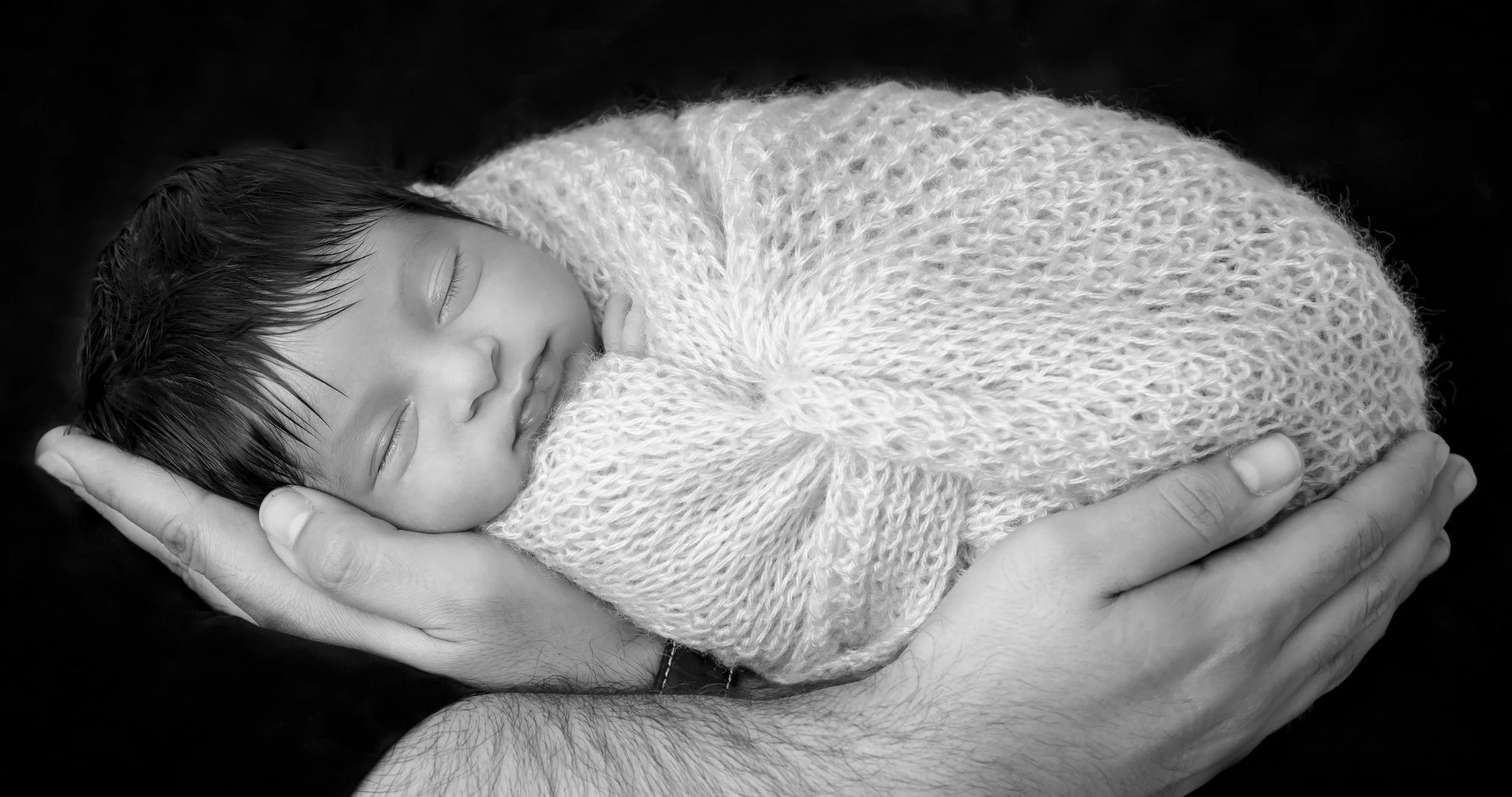 A person holding a sleeping child wrapped in a knitted blanket, with both appearing peaceful and content.