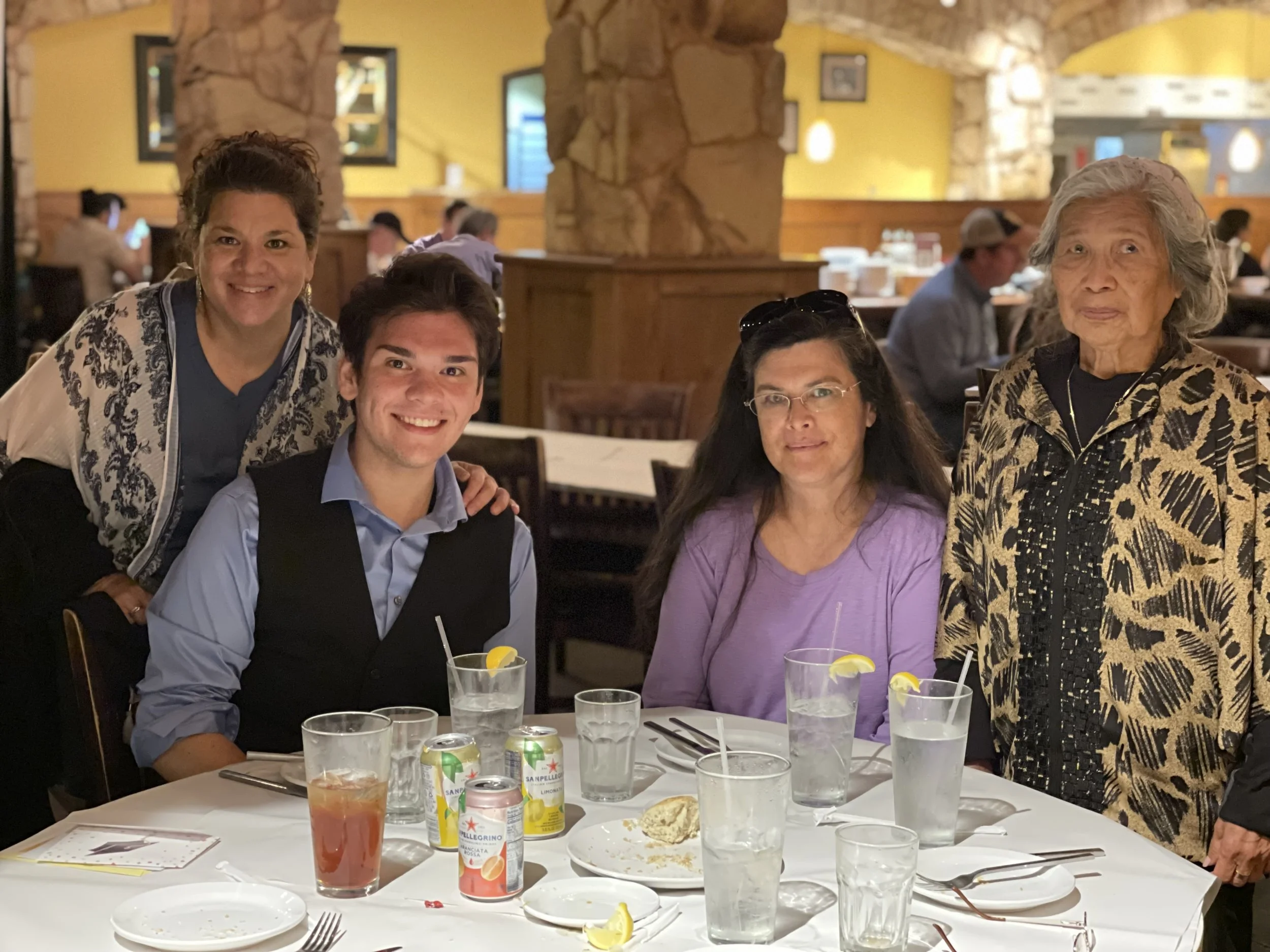 A group of four people posing around a restaurant table with drinks and plates. The setting is casual and friendly.