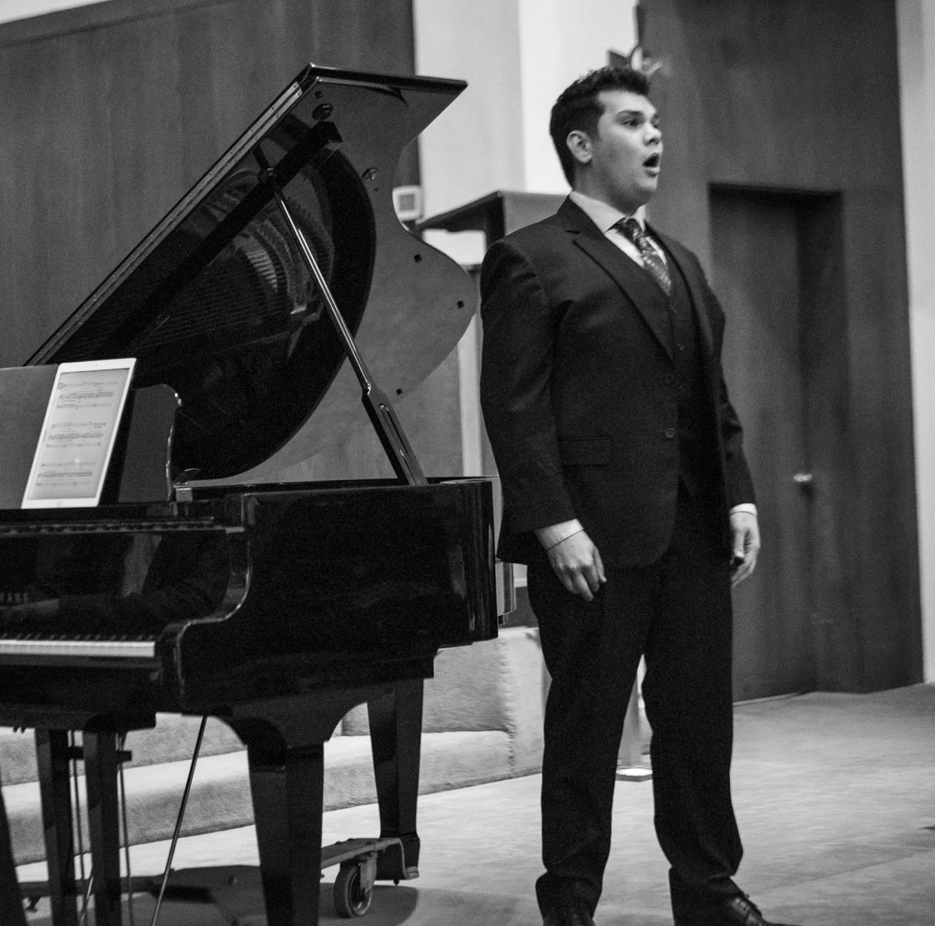 Asa Ambrose sings with Vision Possible Charity Concerts. A man in a suit singing beside a grand piano.