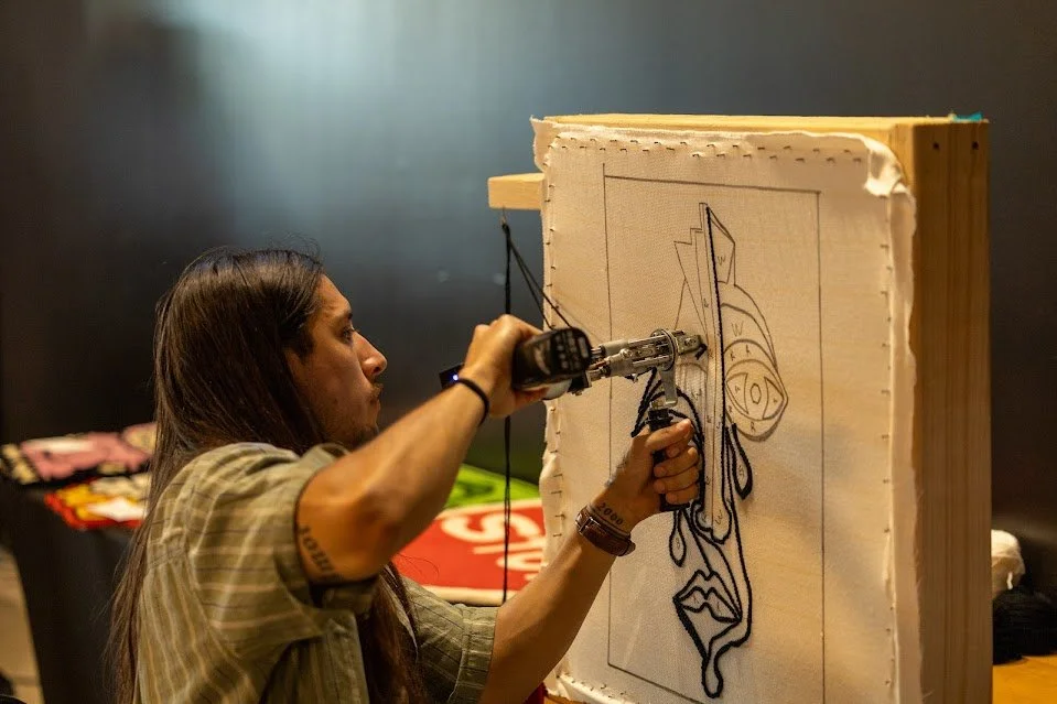 A woman using a robotic arm to draw on a large wood panel with a cartoon-style drawing.
