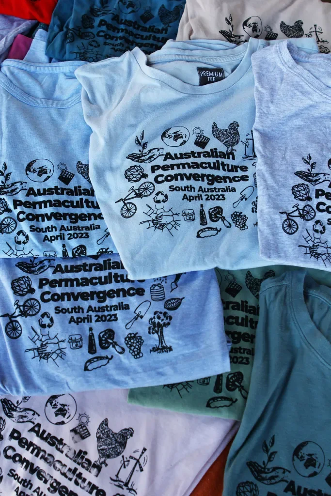A pile of t-shirts printed with the words: Australian Permaculture Convergence
