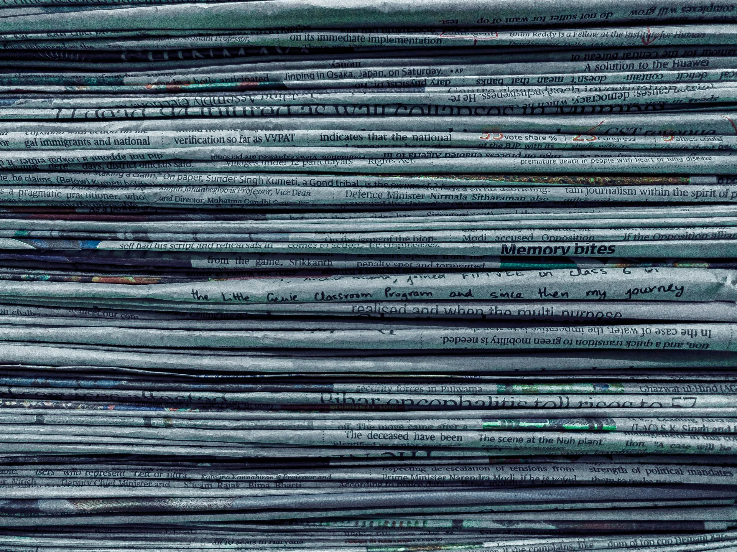 A stack of folded newspapers piled on top of each other, with some visible headlines and articles.