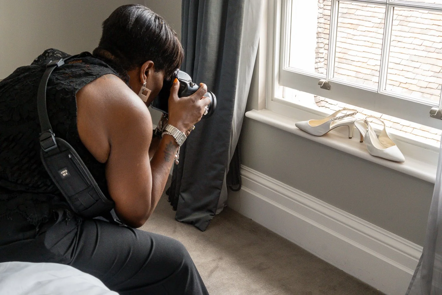 Woman taking a photograph of white high-heeled wedding shoes on a windowsill