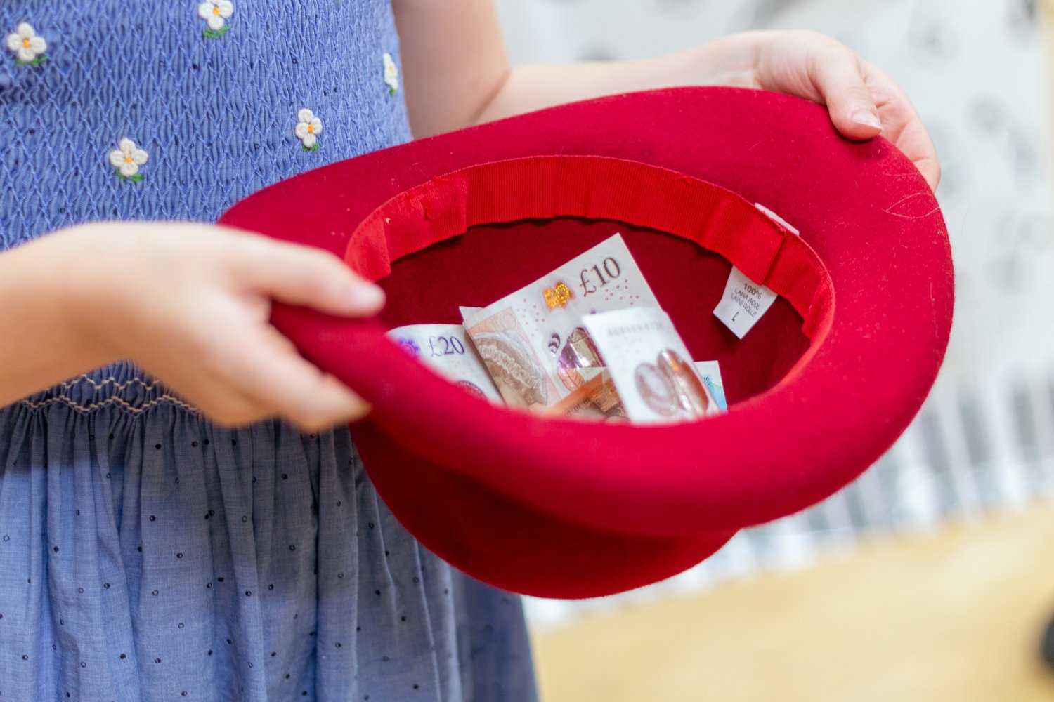 Person holding a red hat with British banknotes inside, including a £10 note.