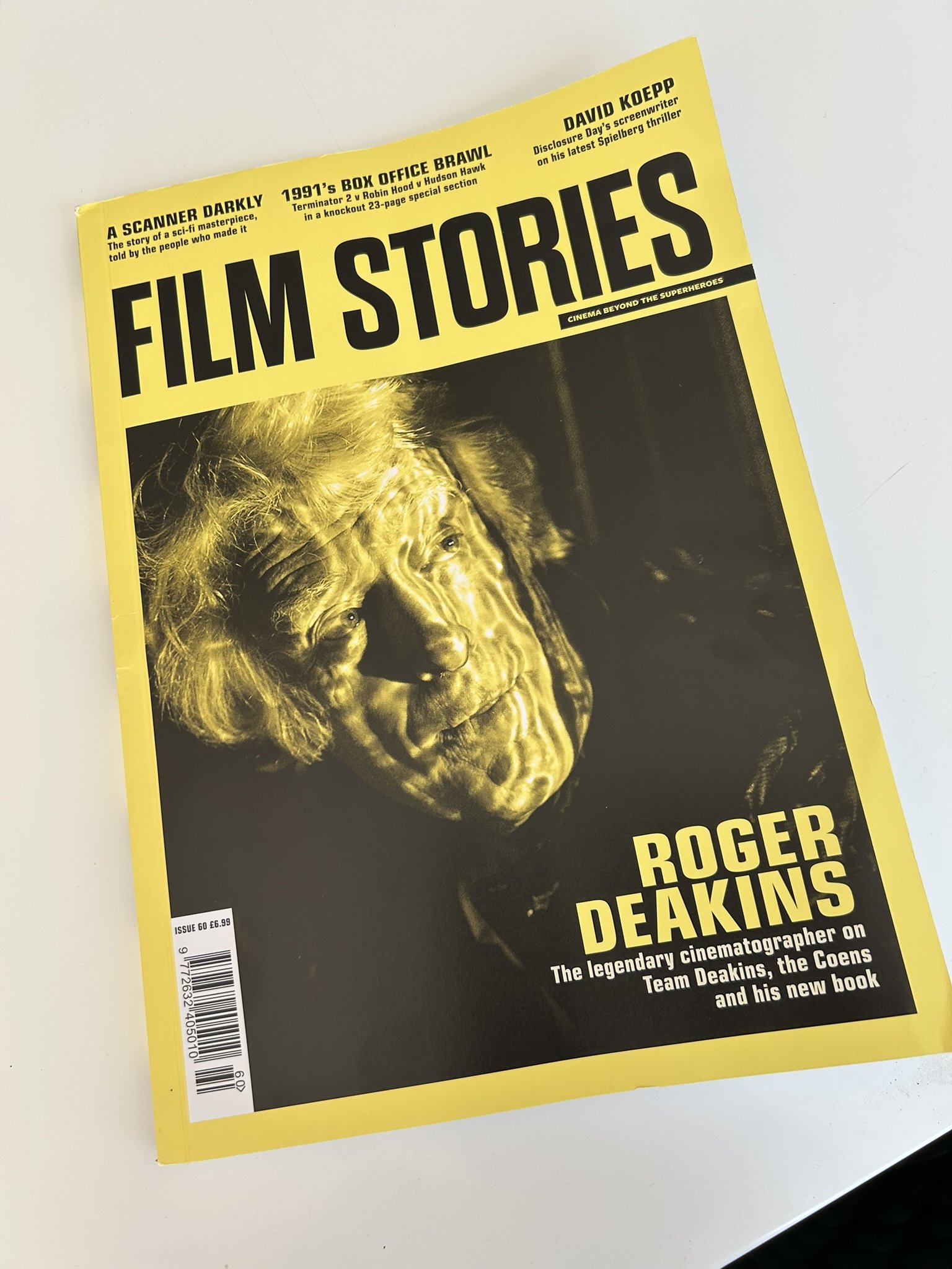 A yellow magazine cover featuring a black and white portrait of Roger Deakins, a renowned cinematographer, with bold black text . The title of the magazine is Film Stories.