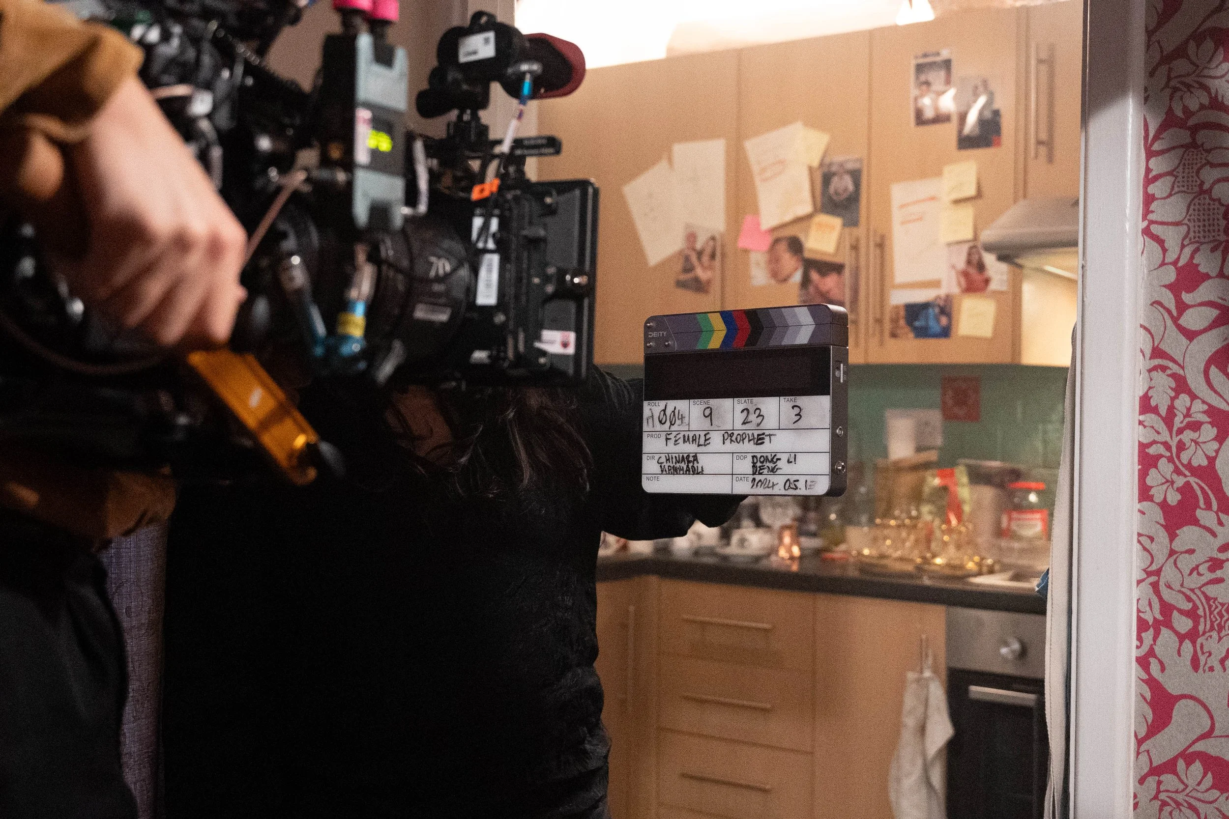 A film crew shooting a scene in a kitchen, with a focus on a clapperboard and a camera operator.
