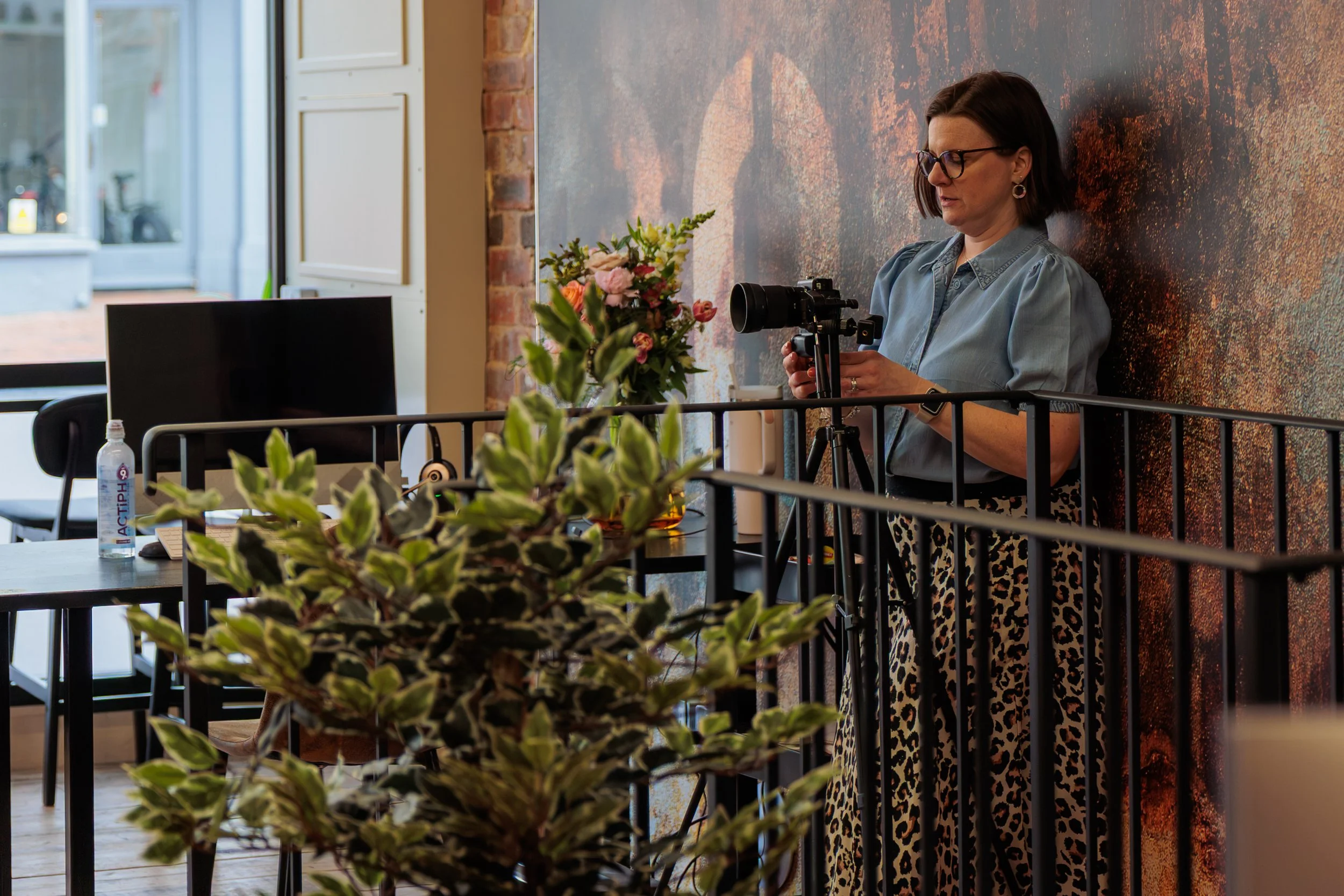 A photographer standing behind railing and a plant checks her camera