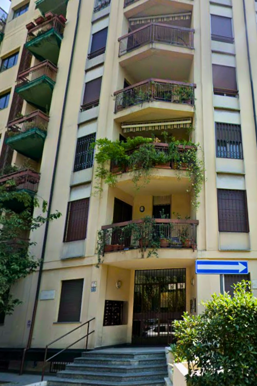 Facciata di un edificio con balconi pieni di piante e un cartello stradale con freccia a destra.