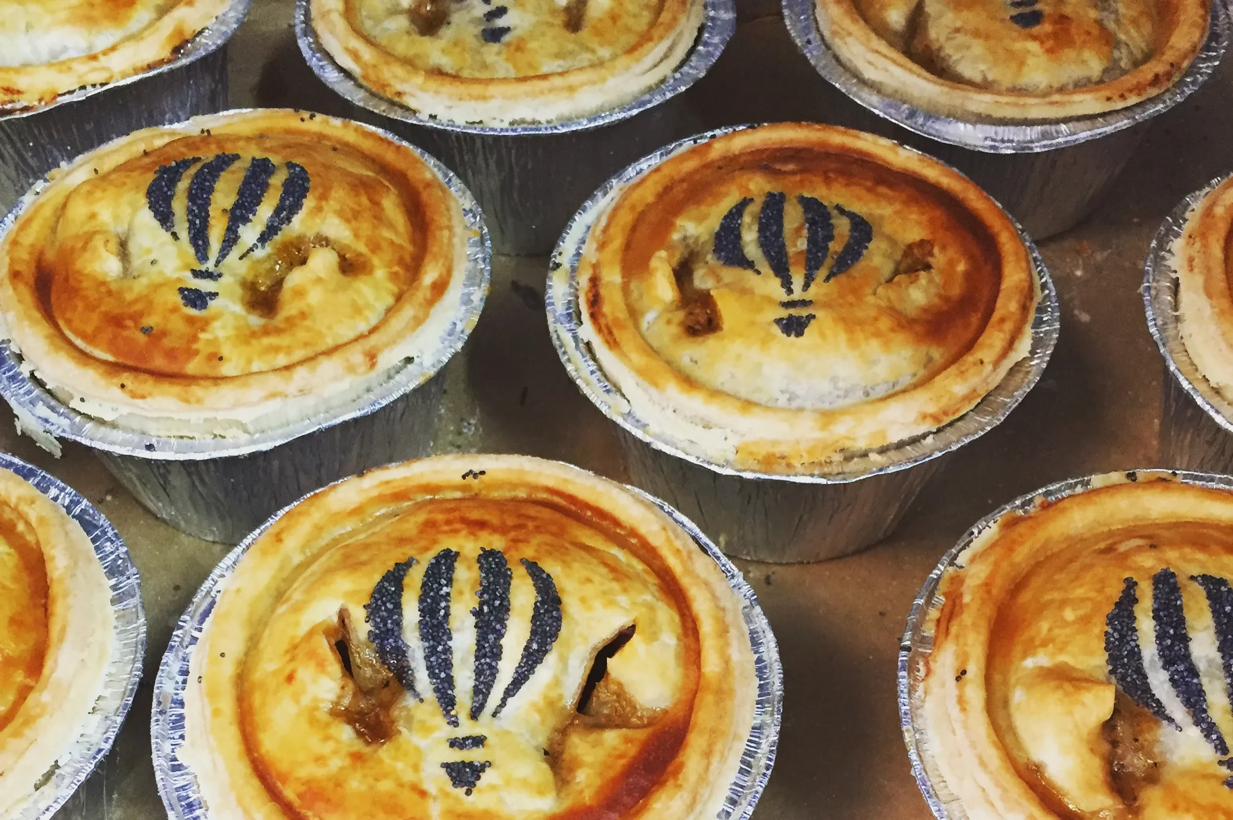Personalized individual pies baked in foil tins with custom pastry art for events by Bristol Pie Society.