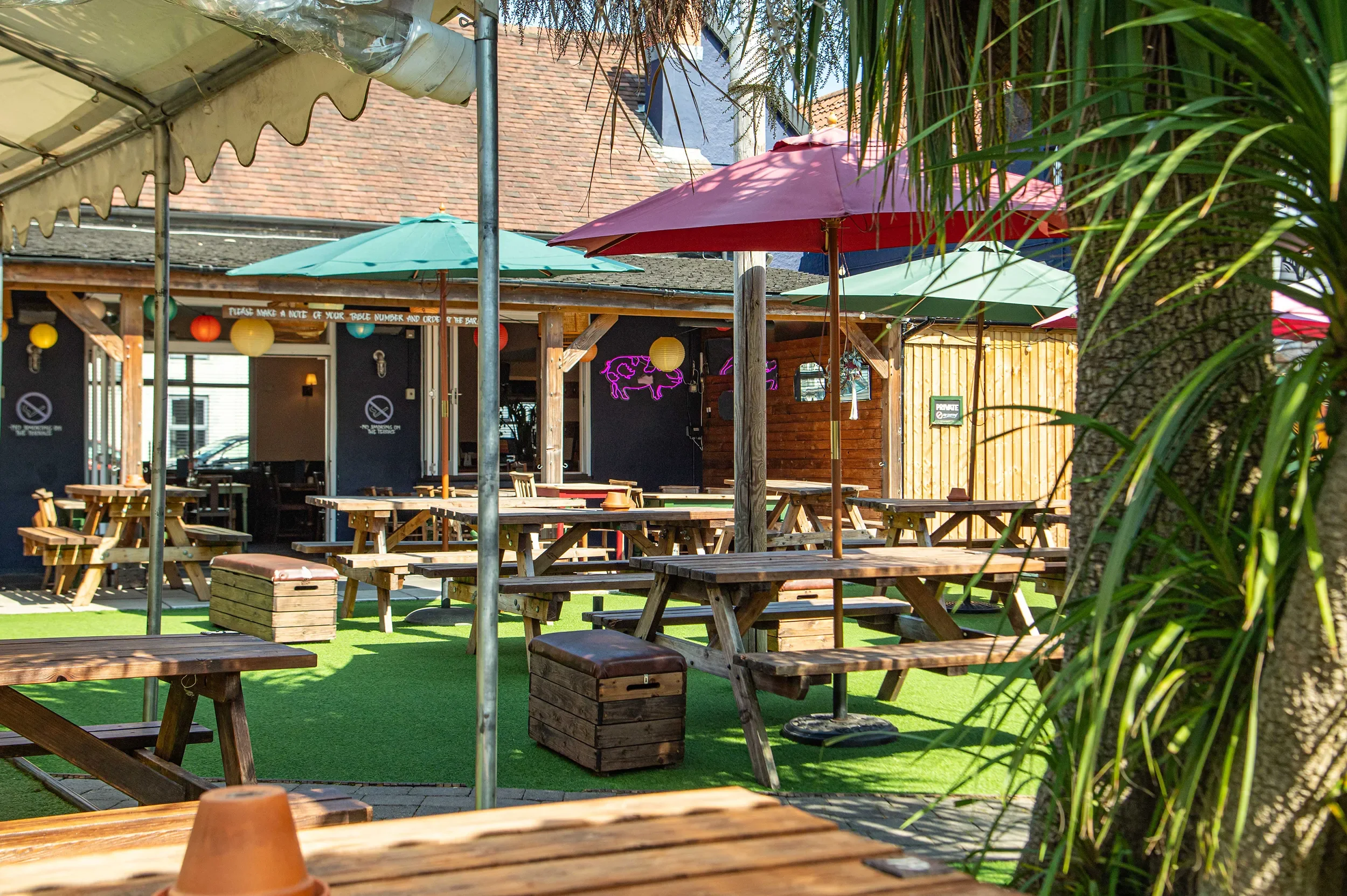 Outdoor marquee and covered terrace overlooking a large pub garden with picnic seating and umbrellas at The Gloucester Old Spot.