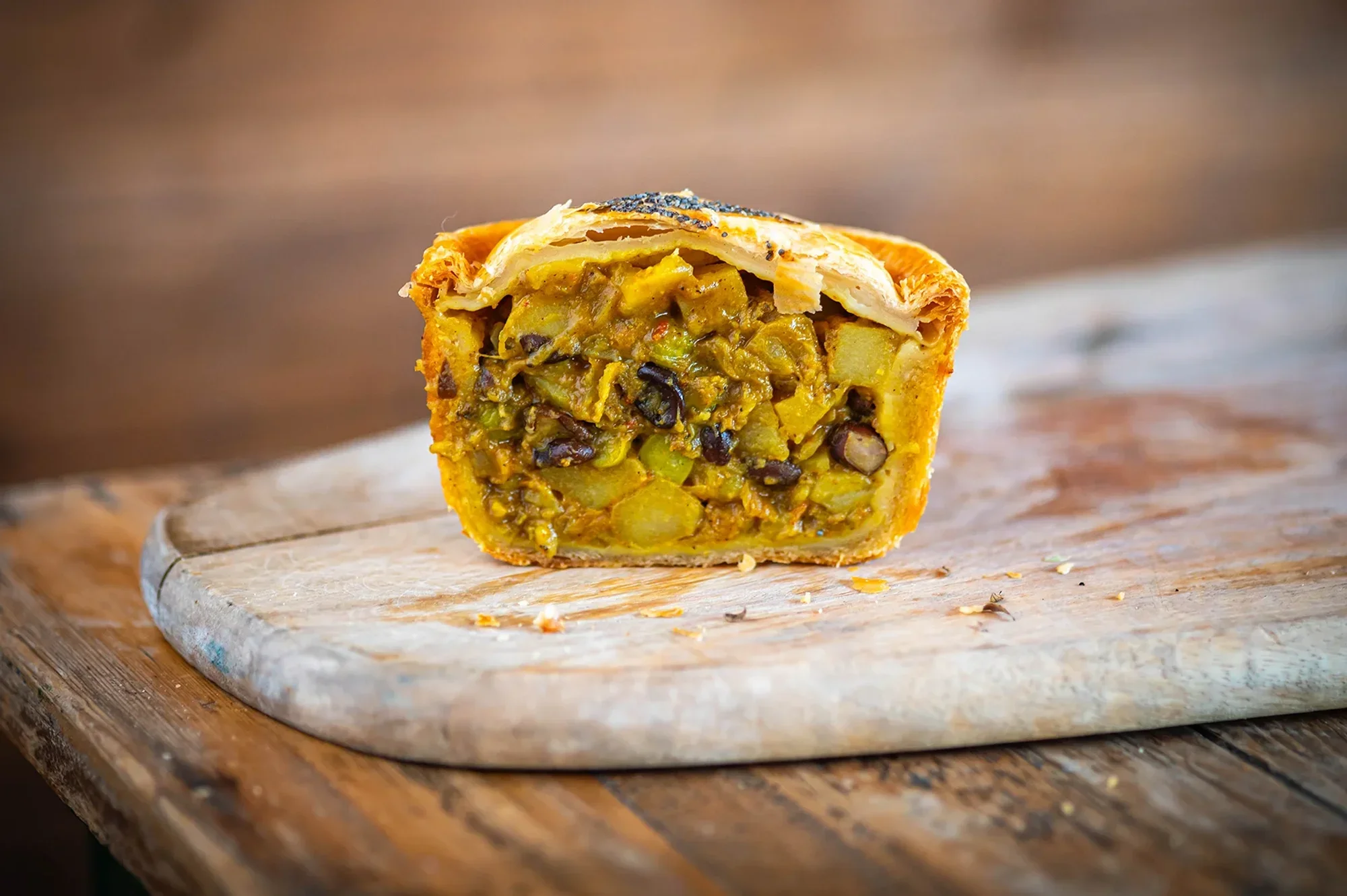 A slice of vegan pie filled with diced vegetables and black beans on a round wooden cutting board with a textured wood background.