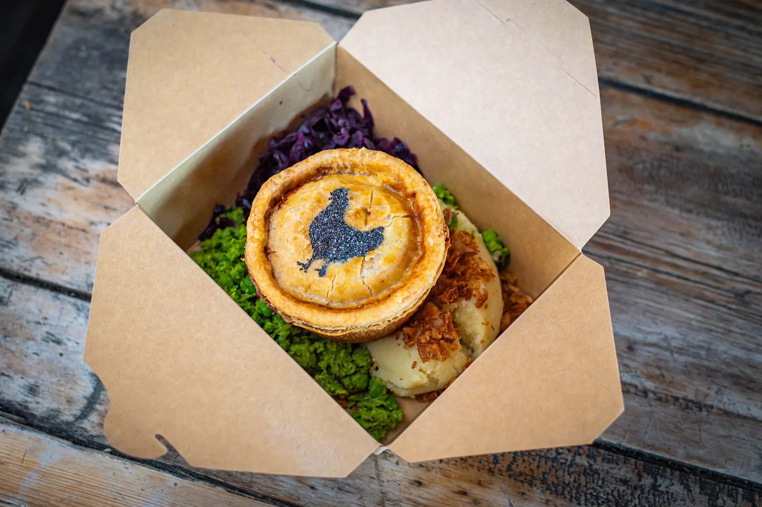 Bristol Pie Society takeaway box from the market stall, featuring an artisan chicken pie with a poppy seed chicken stencil, served with mashed potatoes, crispy onions, mushy peas, and red cabbage.