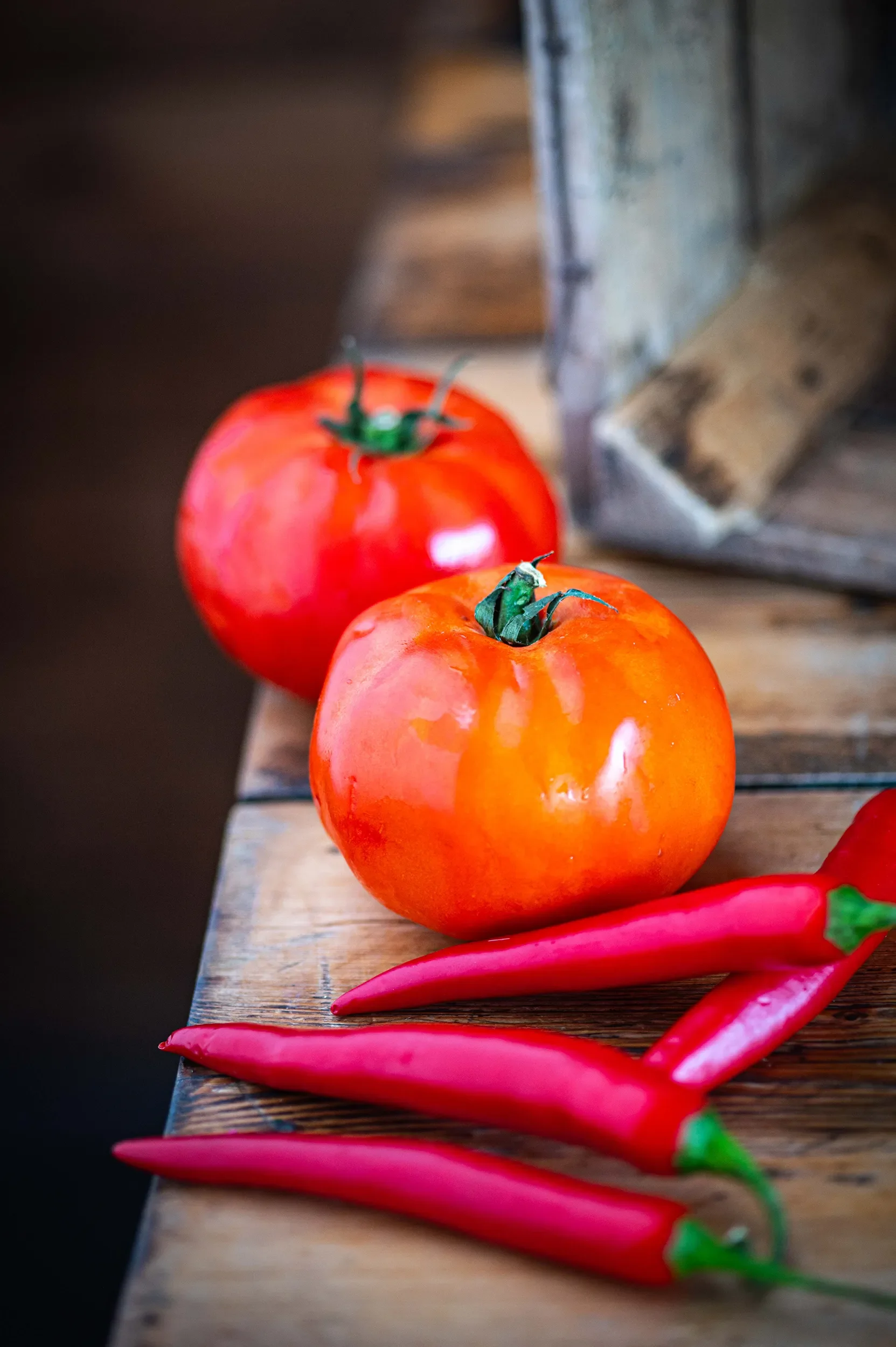 Fresh, vibrant red heirloom tomatoes and bright red chilli peppers resting on a rustic wooden table, representing fresh ingredients.