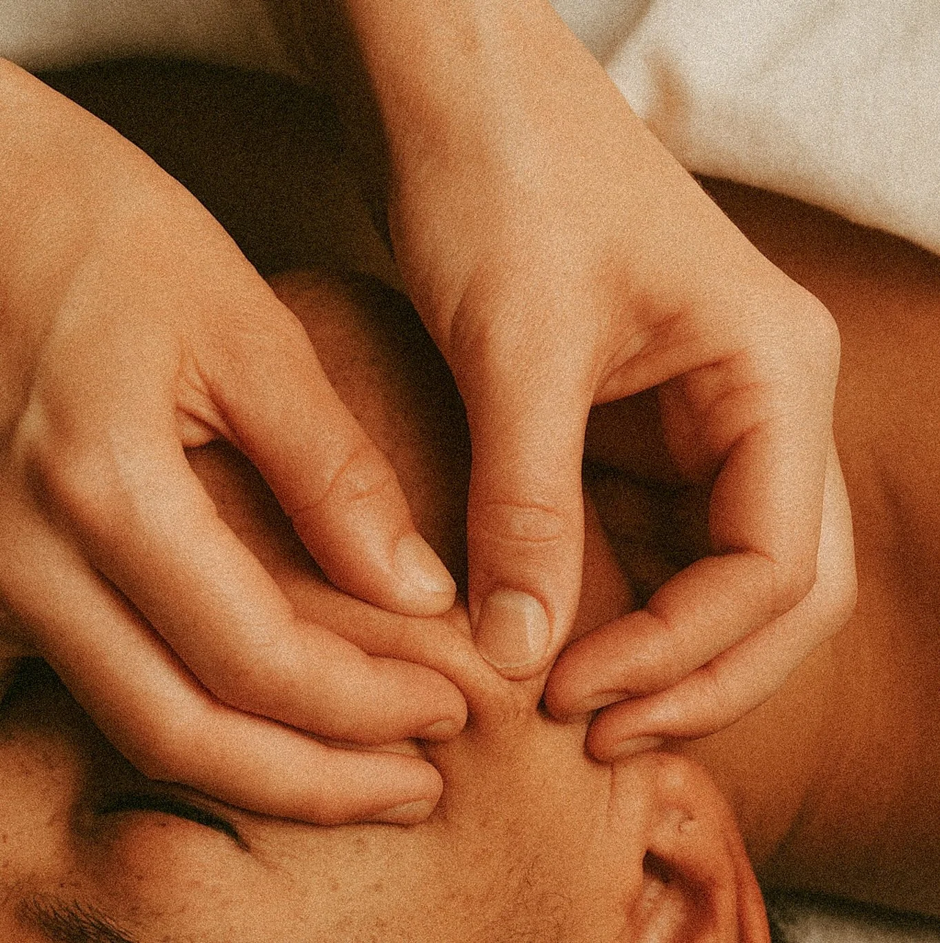 Close-up of hands massaging a person's forehead and temple, promoting lymphatic drainage.