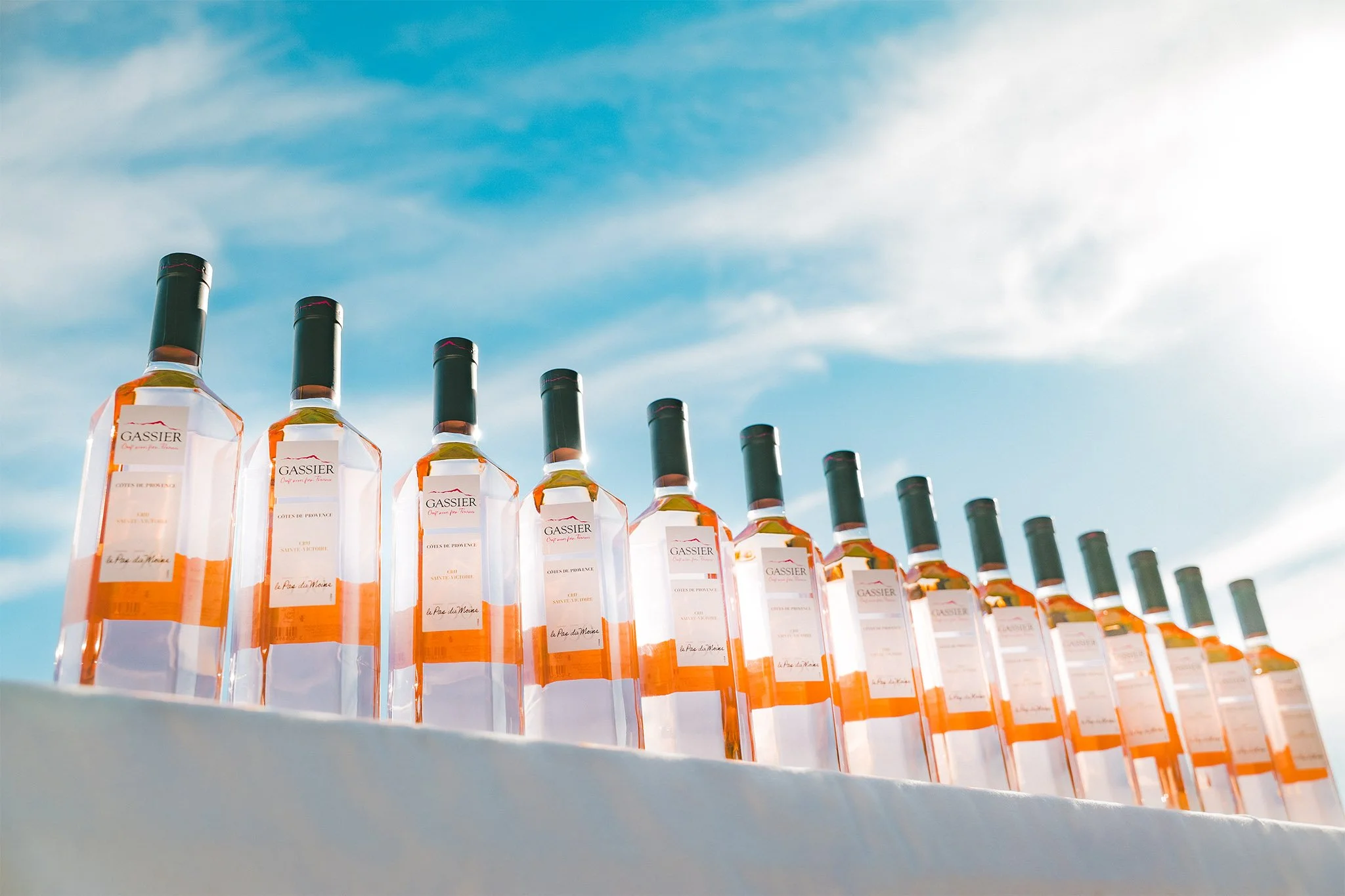 Allignement de bouteilles de rosé pour chateau Gassier. Sous un ciel bleu en provence, esthétique lumineuse et minimaliste. Réalisé dans le cadre d'une campagne de communication visuelle.